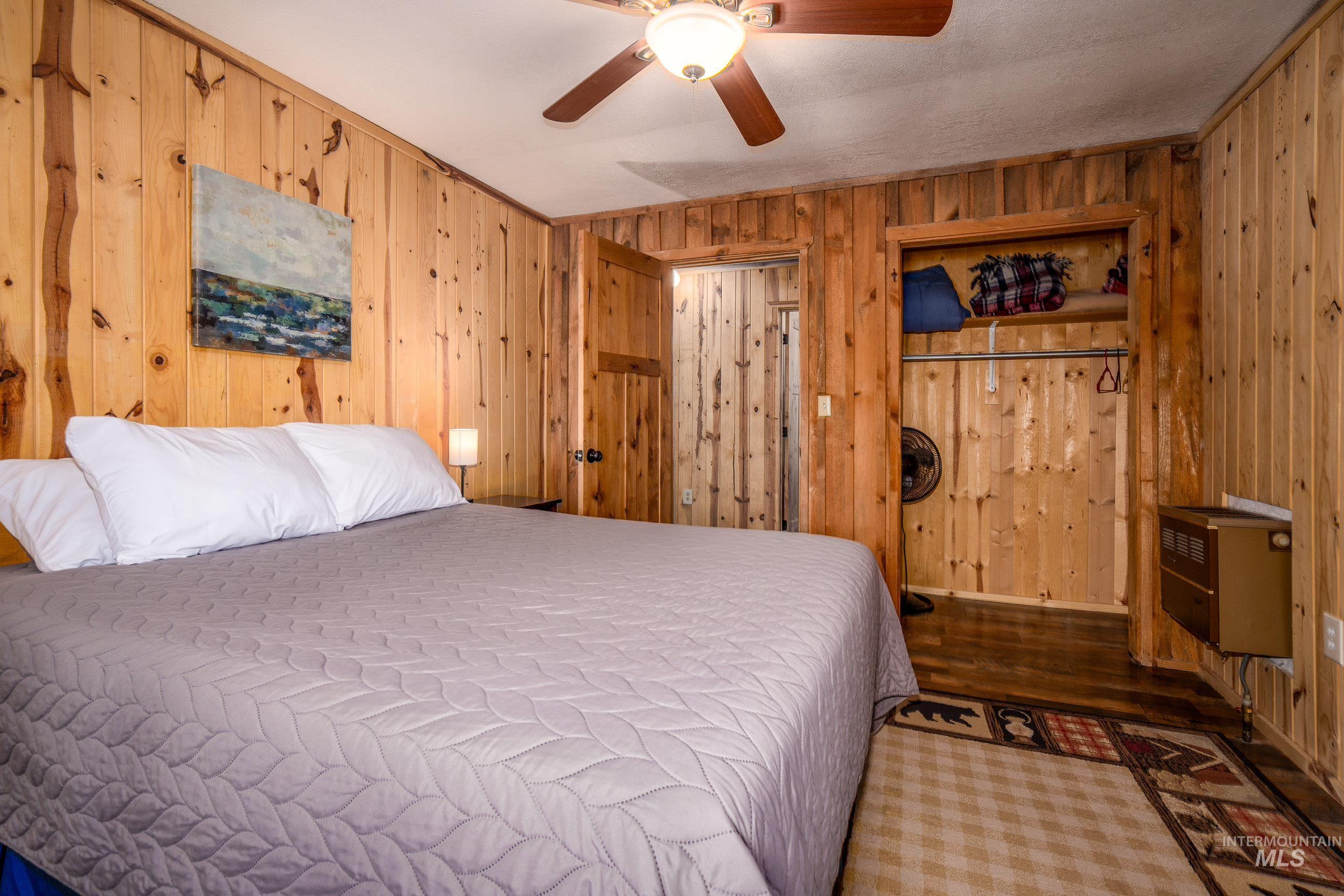 Bedroom featuring wooden walls, a ceiling fan, wood finished floors, and heating unit