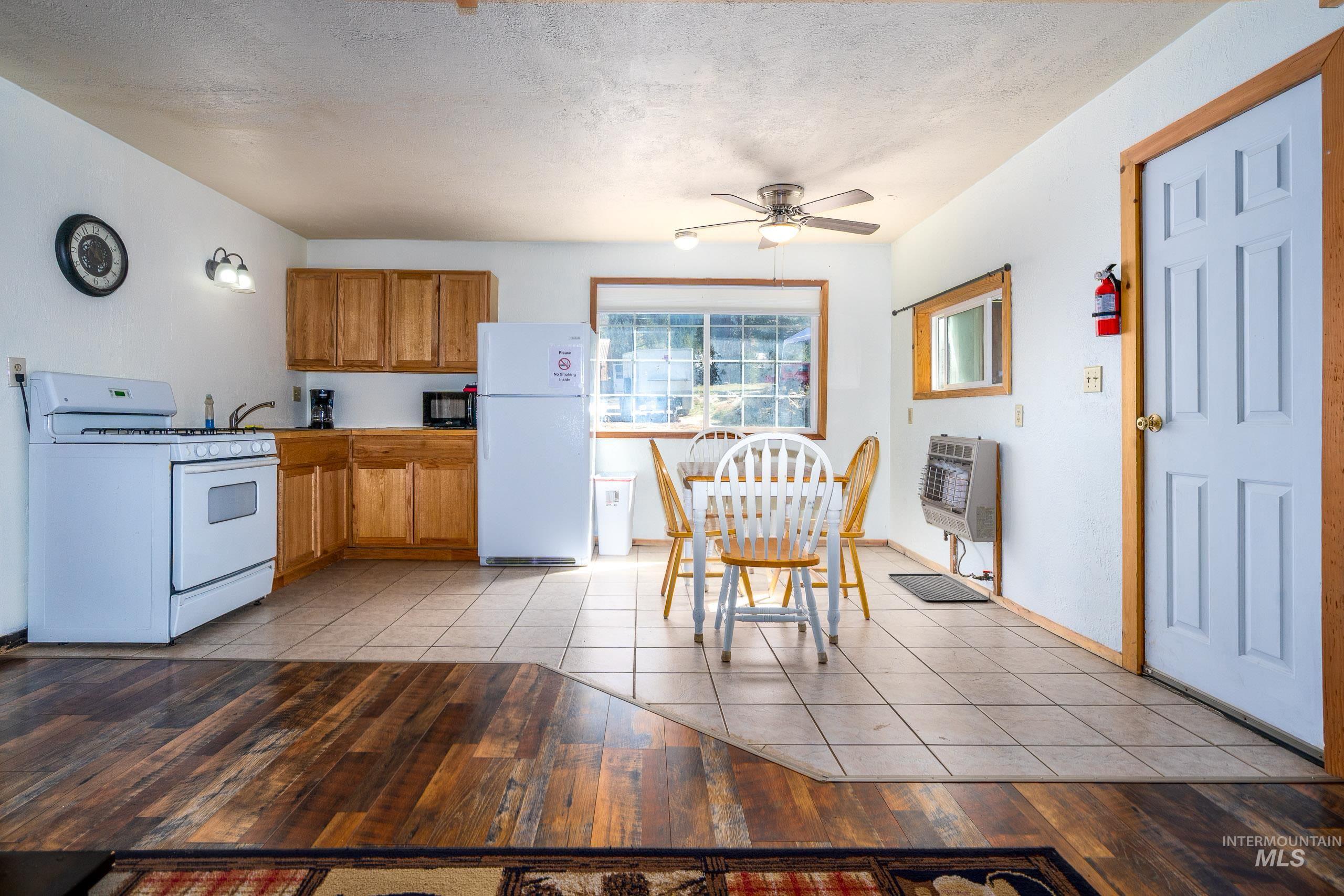 Kitchen featuring brown cabinets, white appliances, light tile patterned flooring, a textured ceiling, and ceiling fan