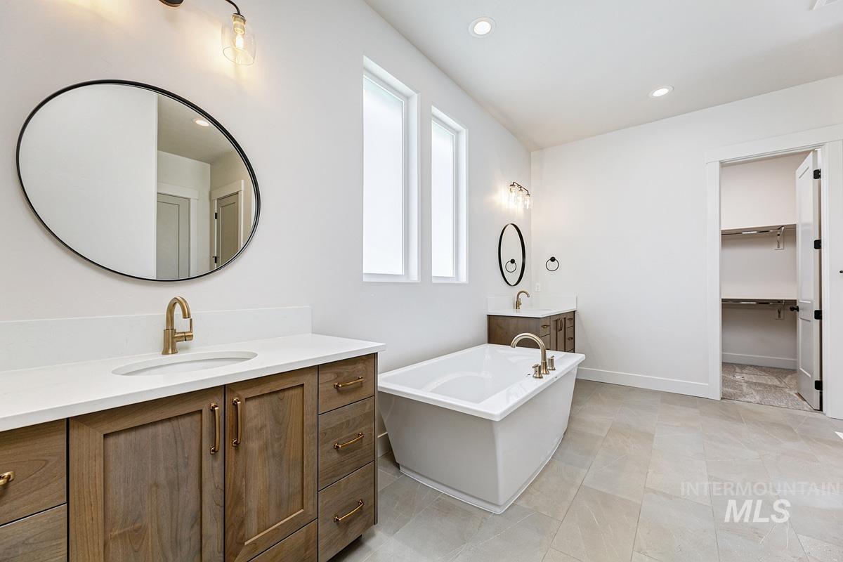 Bathroom featuring recessed lighting, a soaking tub, two vanities, a walk in closet, and light tile patterned floors