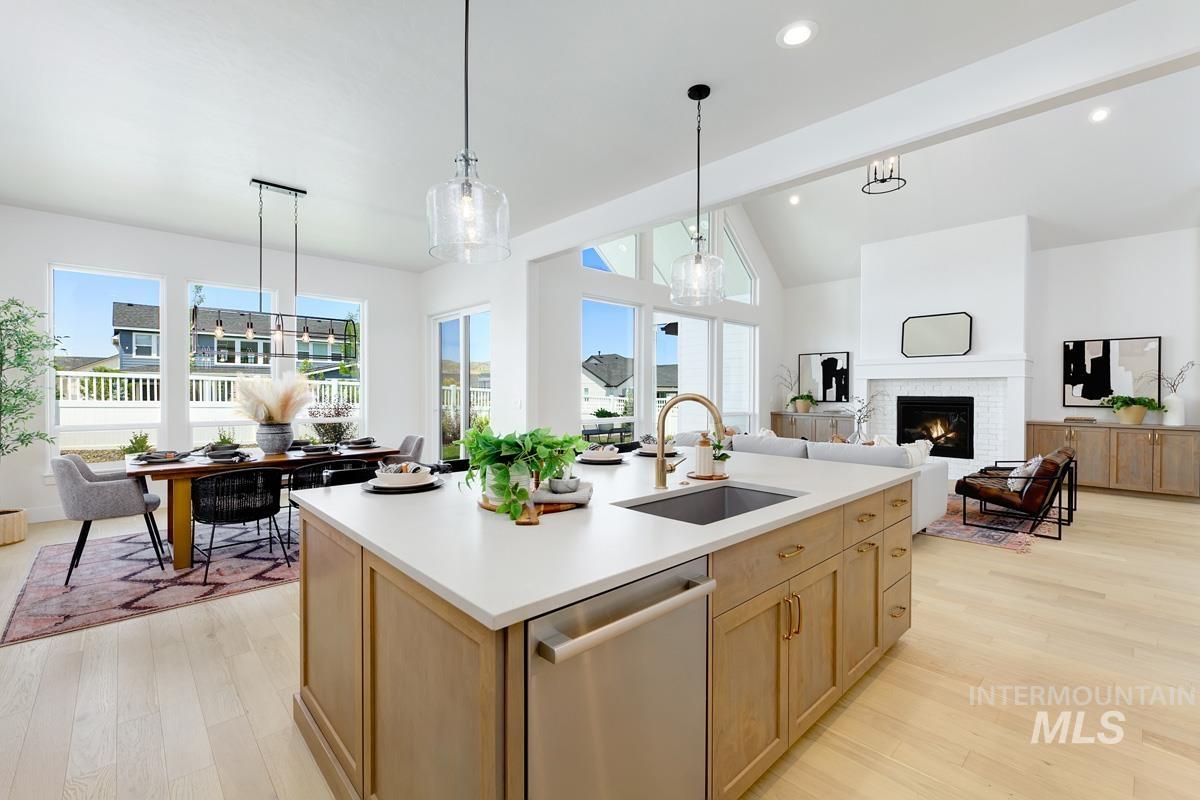 Kitchen with light brown cabinets, dishwasher, a lit fireplace, decorative light fixtures, and light wood-style flooring