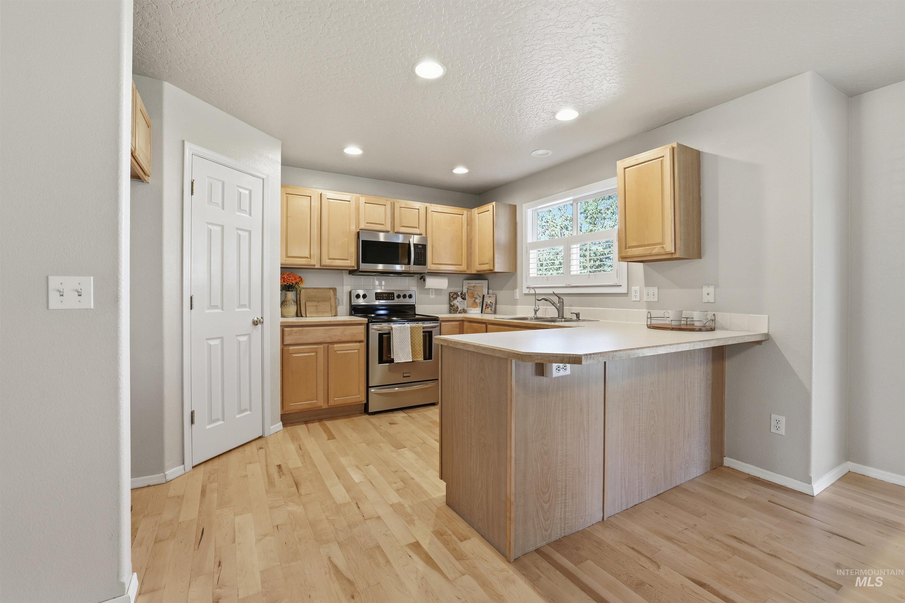 Kitchen with recessed lighting, stainless steel appliances, a peninsula, light countertops, and light wood-style floors