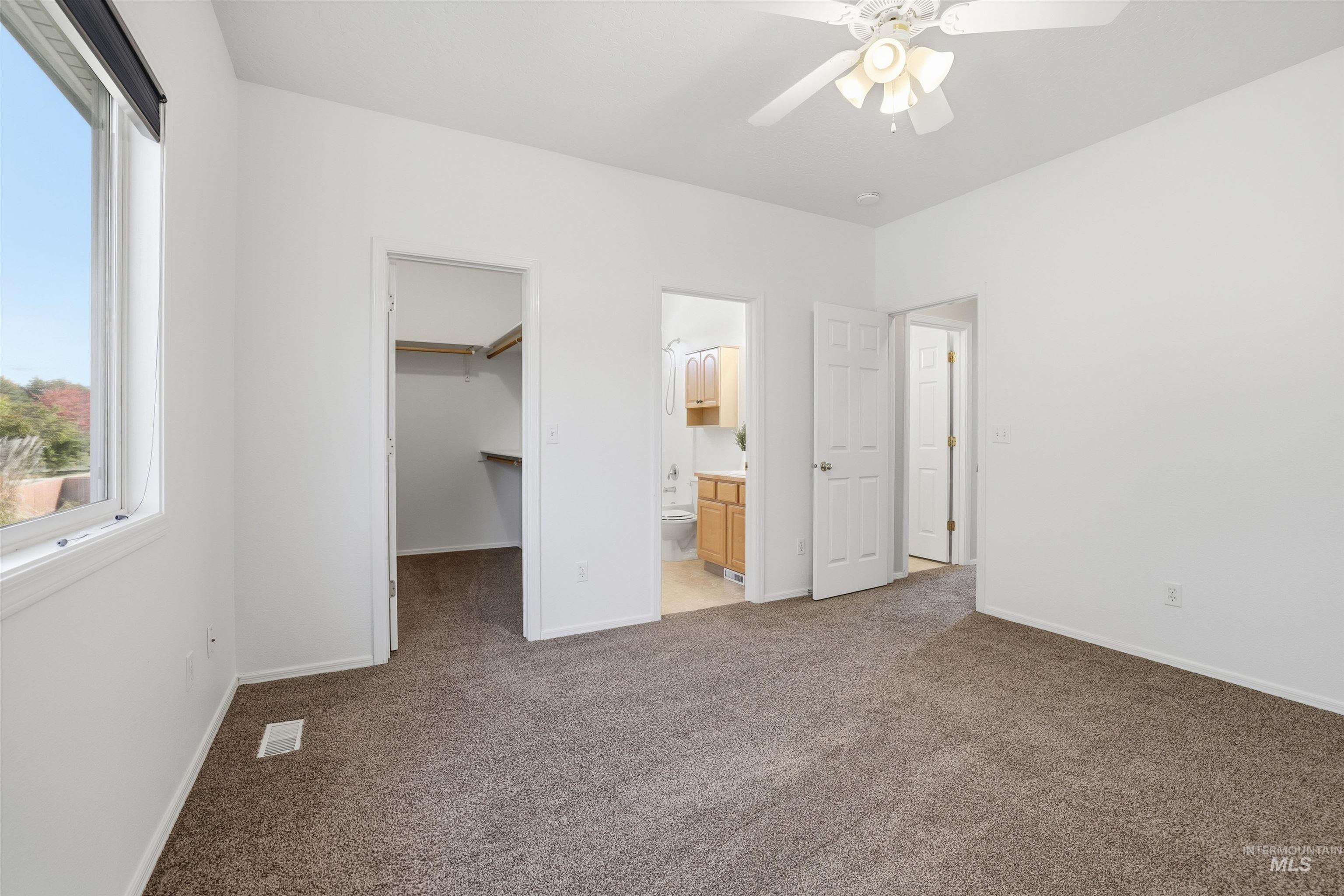 Unfurnished bedroom with light colored carpet, ceiling fan, a walk in closet, and connected bathroom