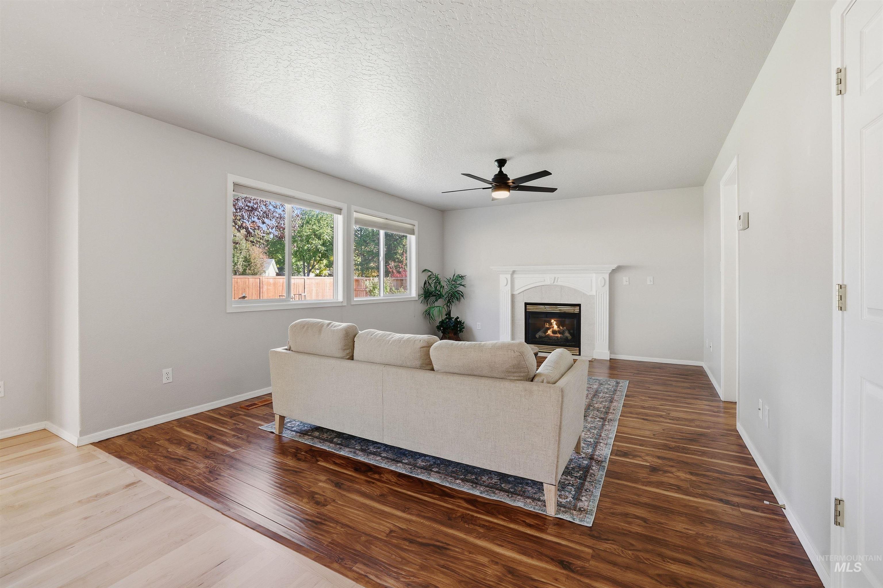 Living room featuring dark wood-type flooring, a glass covered fireplace, a textured ceiling, and a ceiling fan