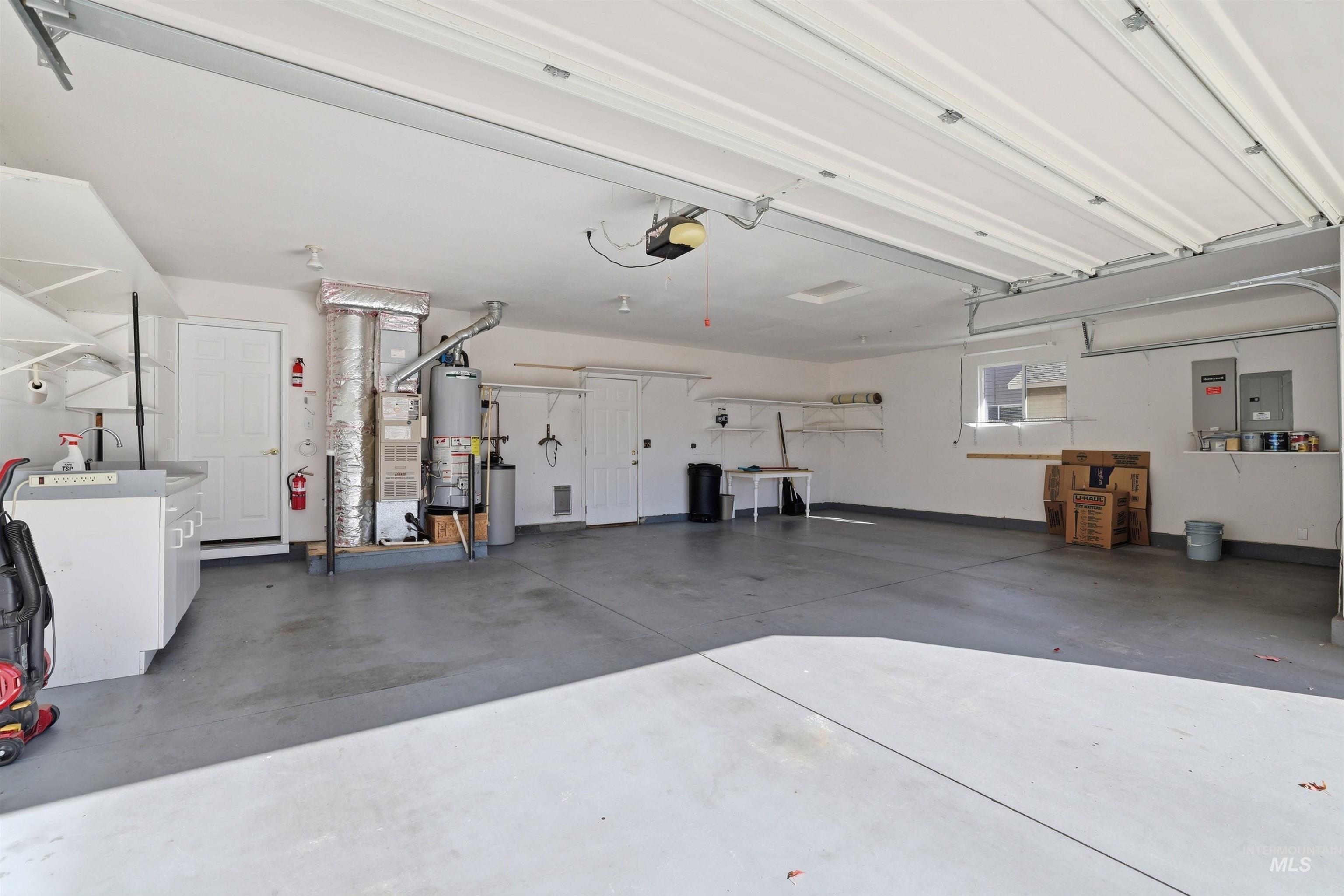 Garage featuring heating unit, electric panel, gas water heater, and a garage door opener