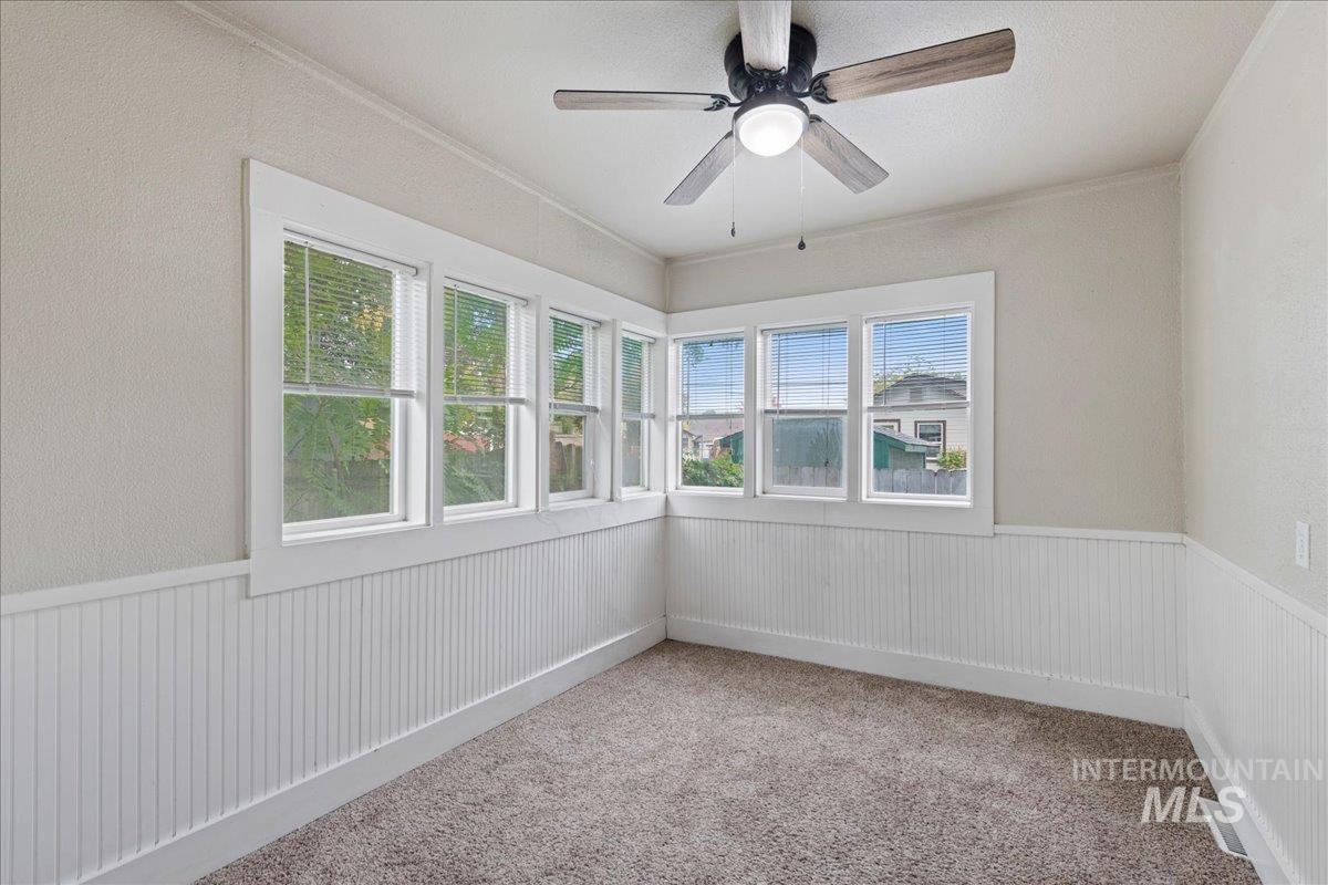 Unfurnished room with light colored carpet, ornamental molding, a ceiling fan, and a wainscoted wall