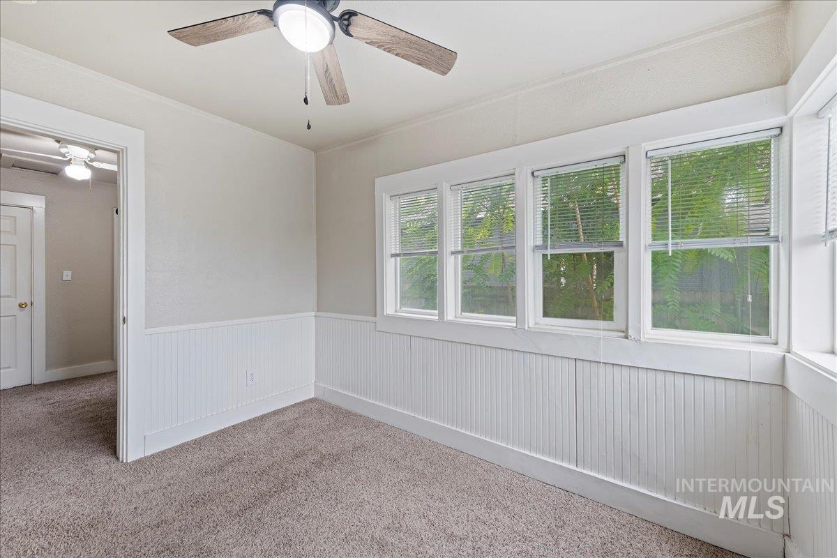 Carpeted empty room featuring crown molding, a wainscoted wall, and ceiling fan