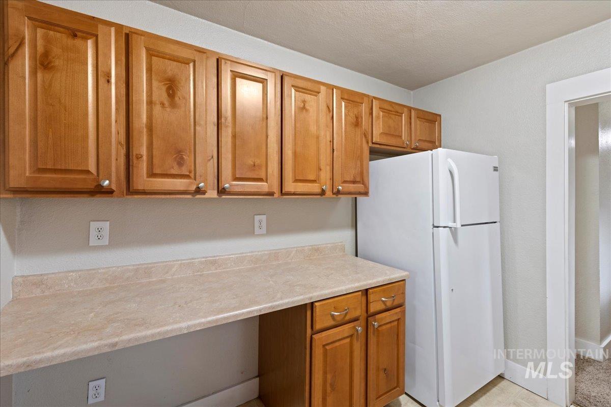 Kitchen featuring light countertops, freestanding refrigerator, brown cabinets, and a textured ceiling