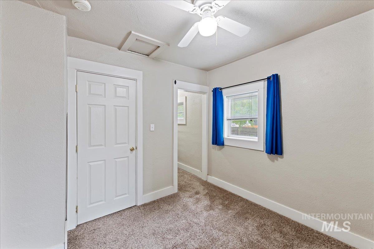 Unfurnished bedroom with attic access, a textured wall, light colored carpet, and a ceiling fan
