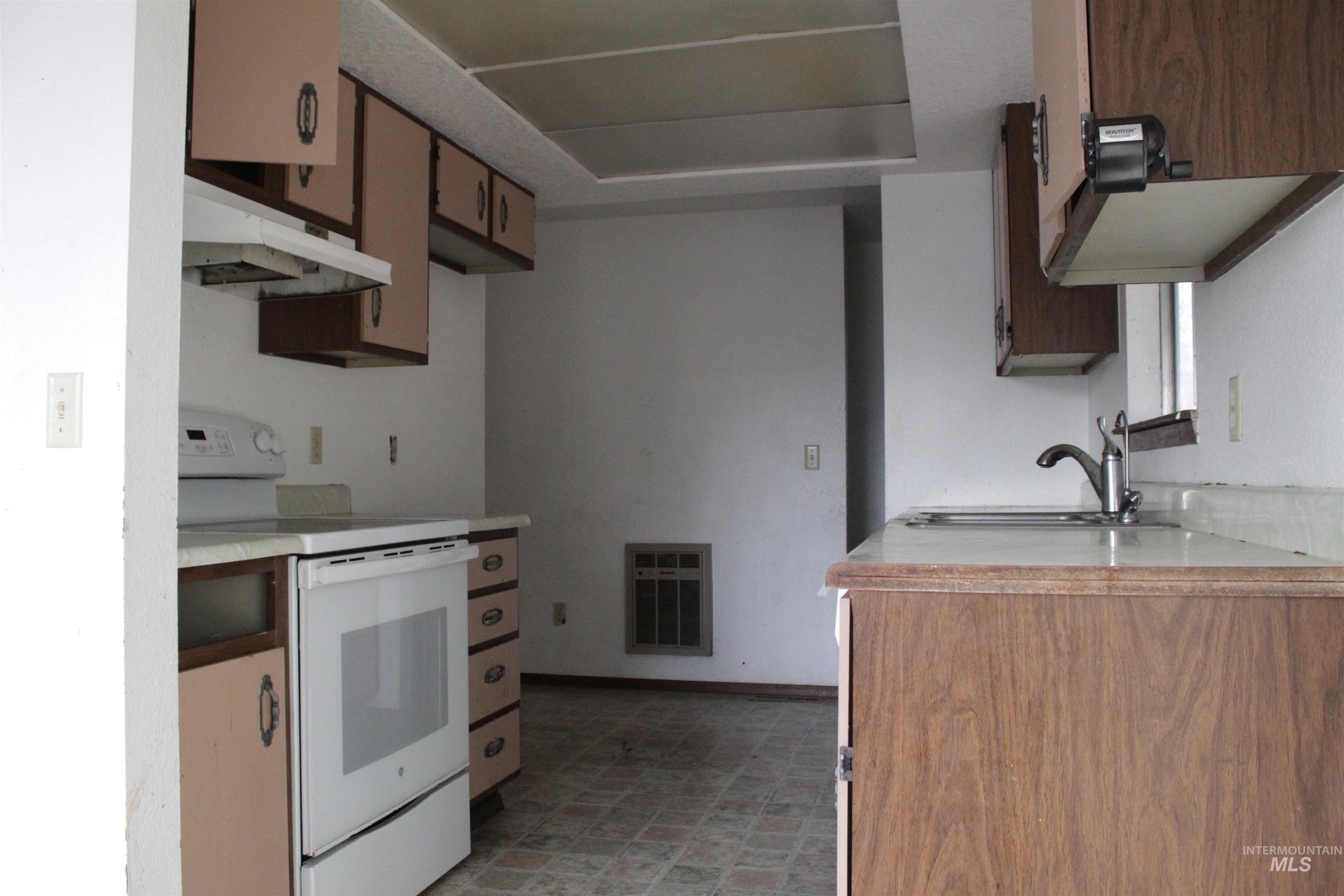 Kitchen with electric range, light countertops, heating unit, light floors, and wood finish cabinetry