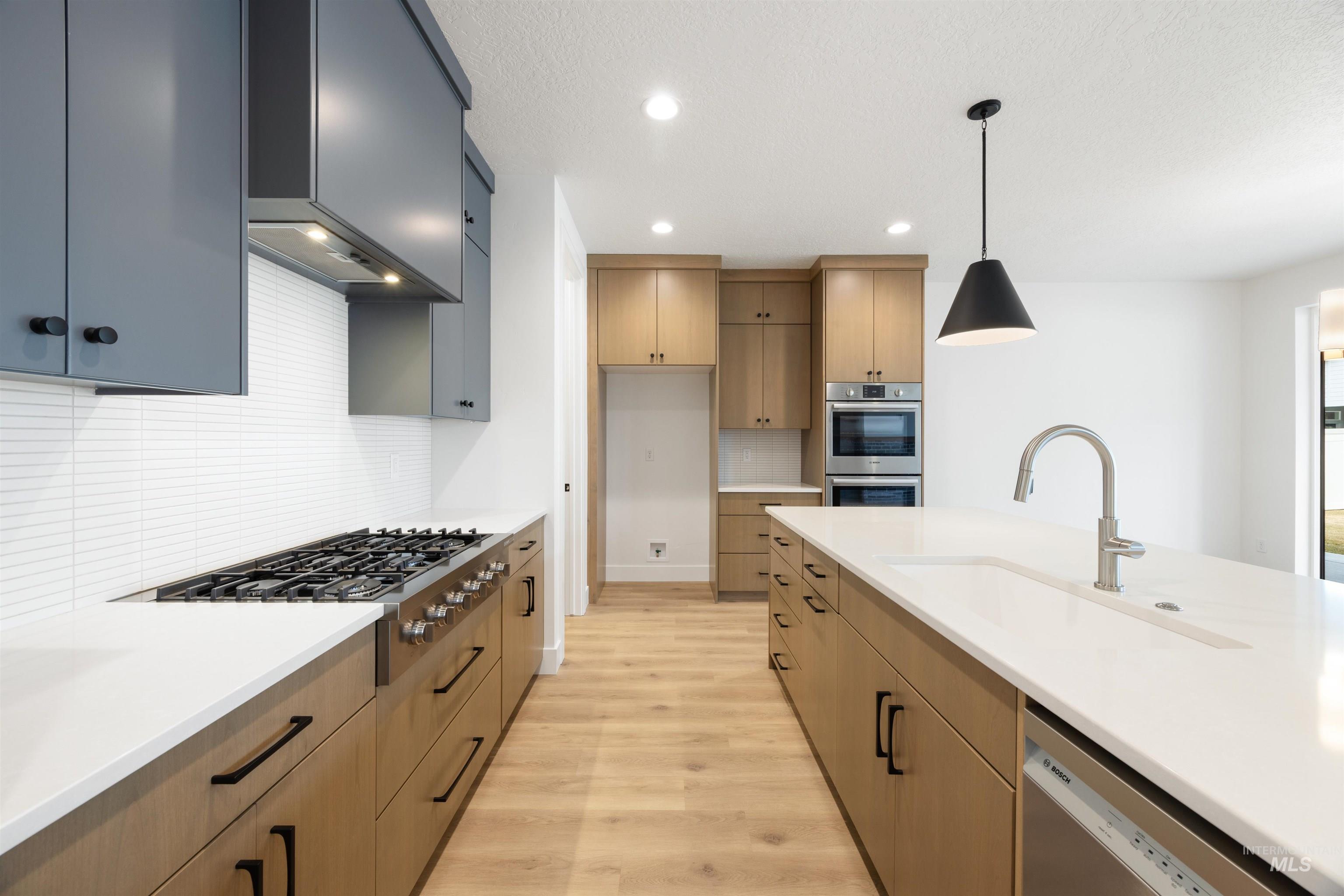 Kitchen with light wood finished floors, stainless steel appliances, decorative light fixtures, and light stone countertops