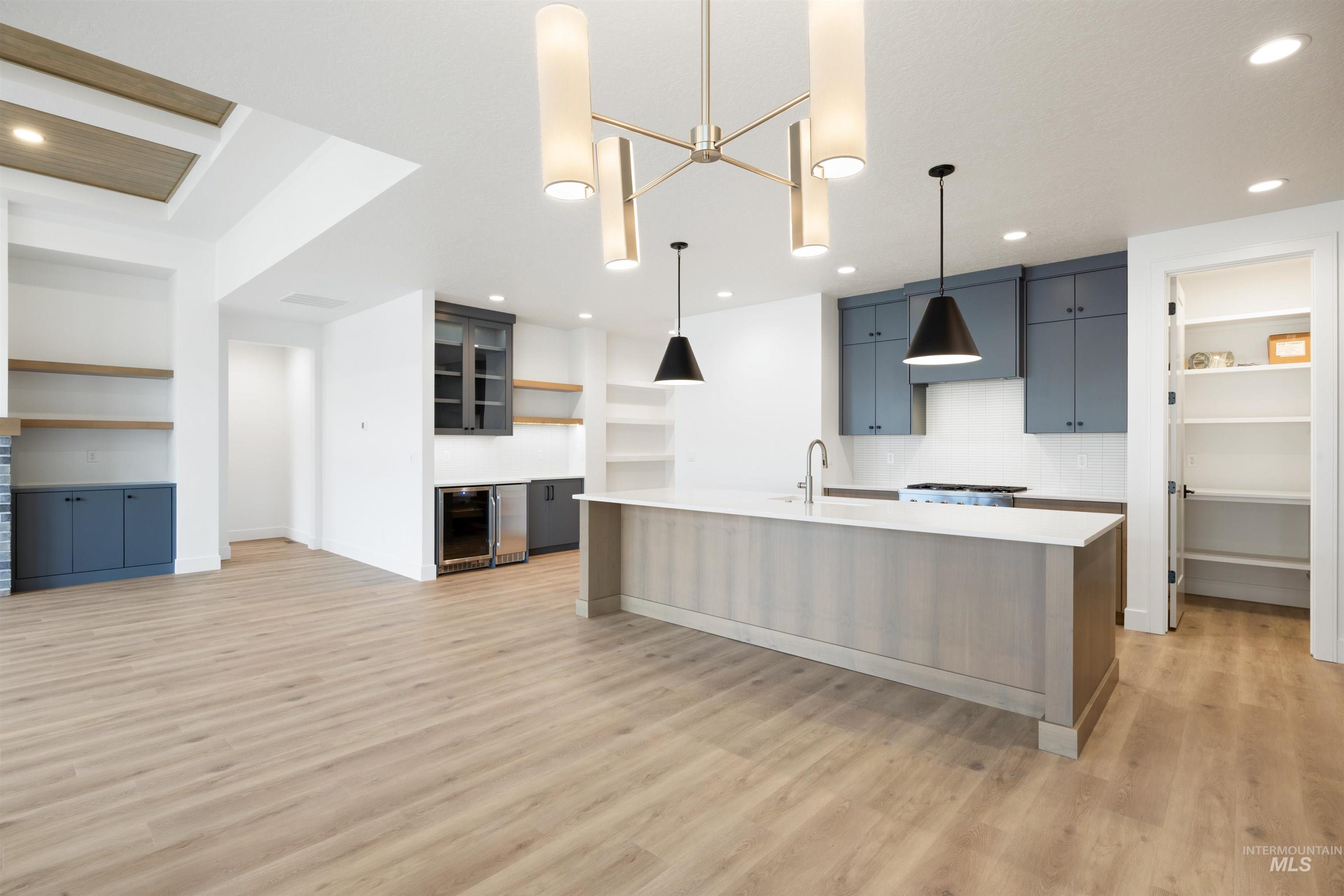 Kitchen with open shelves, a large island with sink, decorative light fixtures, light wood-style floors, and built in shelves