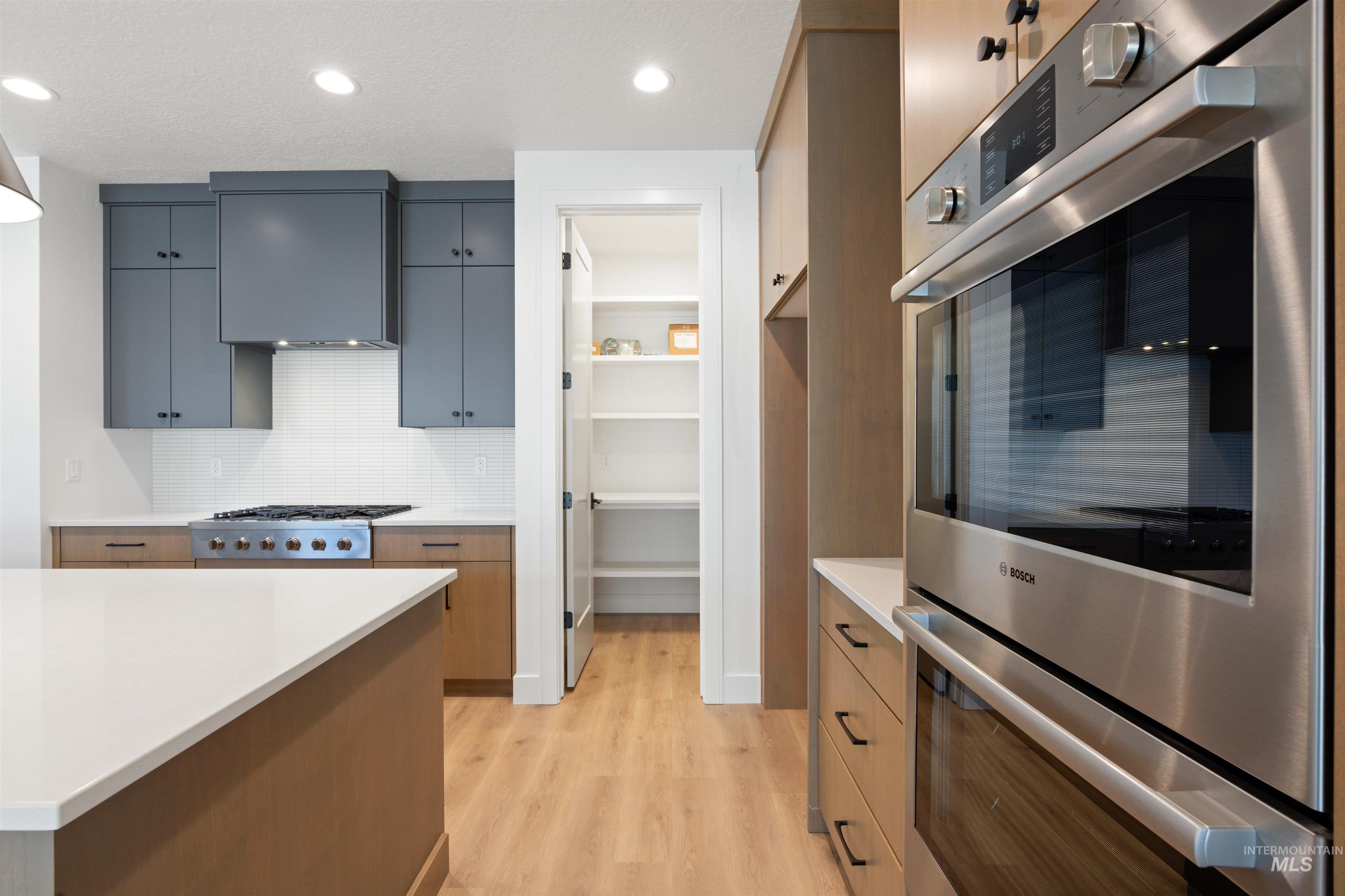 Kitchen with stainless steel appliances, decorative backsplash, light wood-type flooring, extractor fan, and recessed lighting