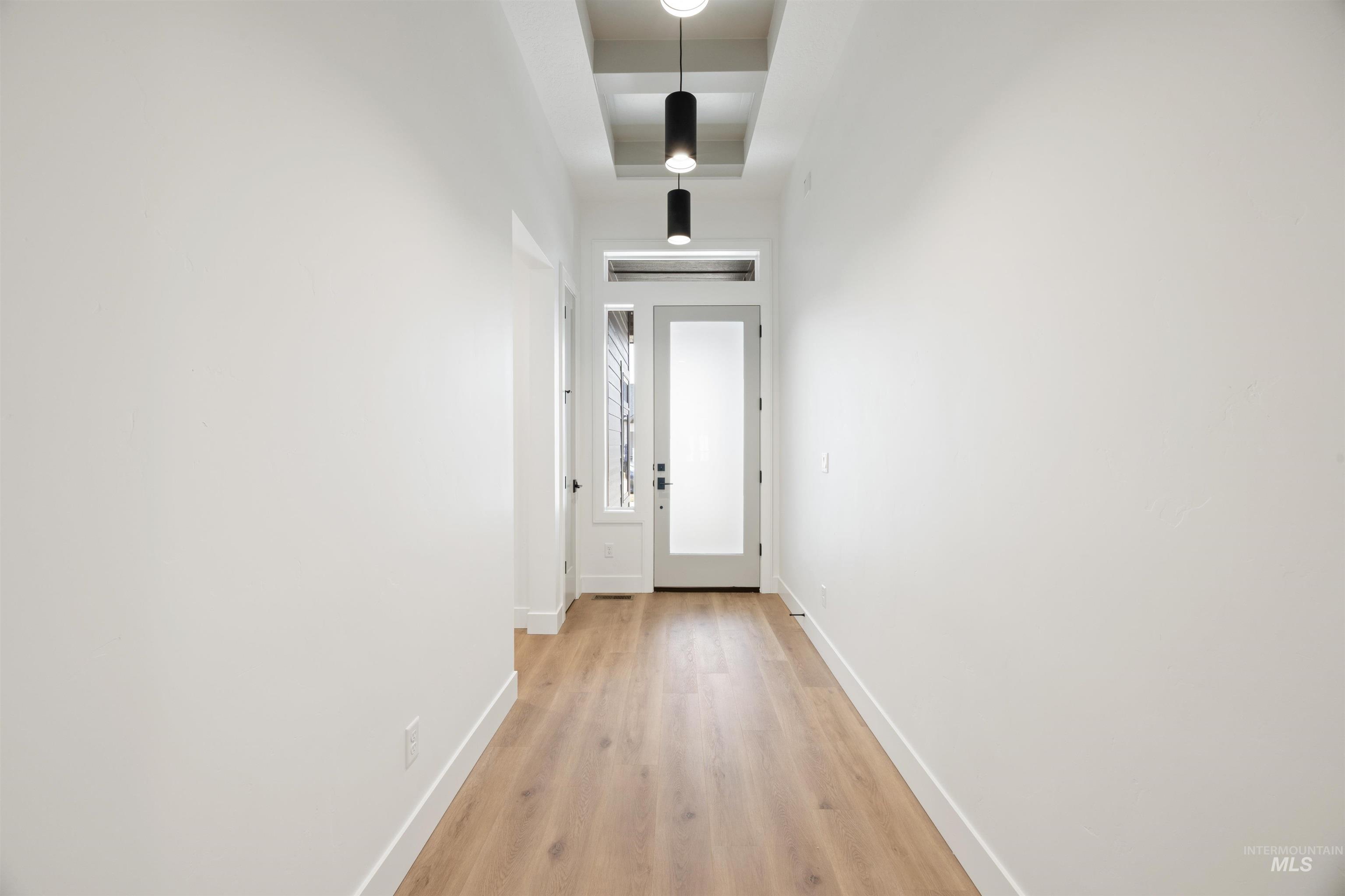 Hall with a raised ceiling and light wood-style floors