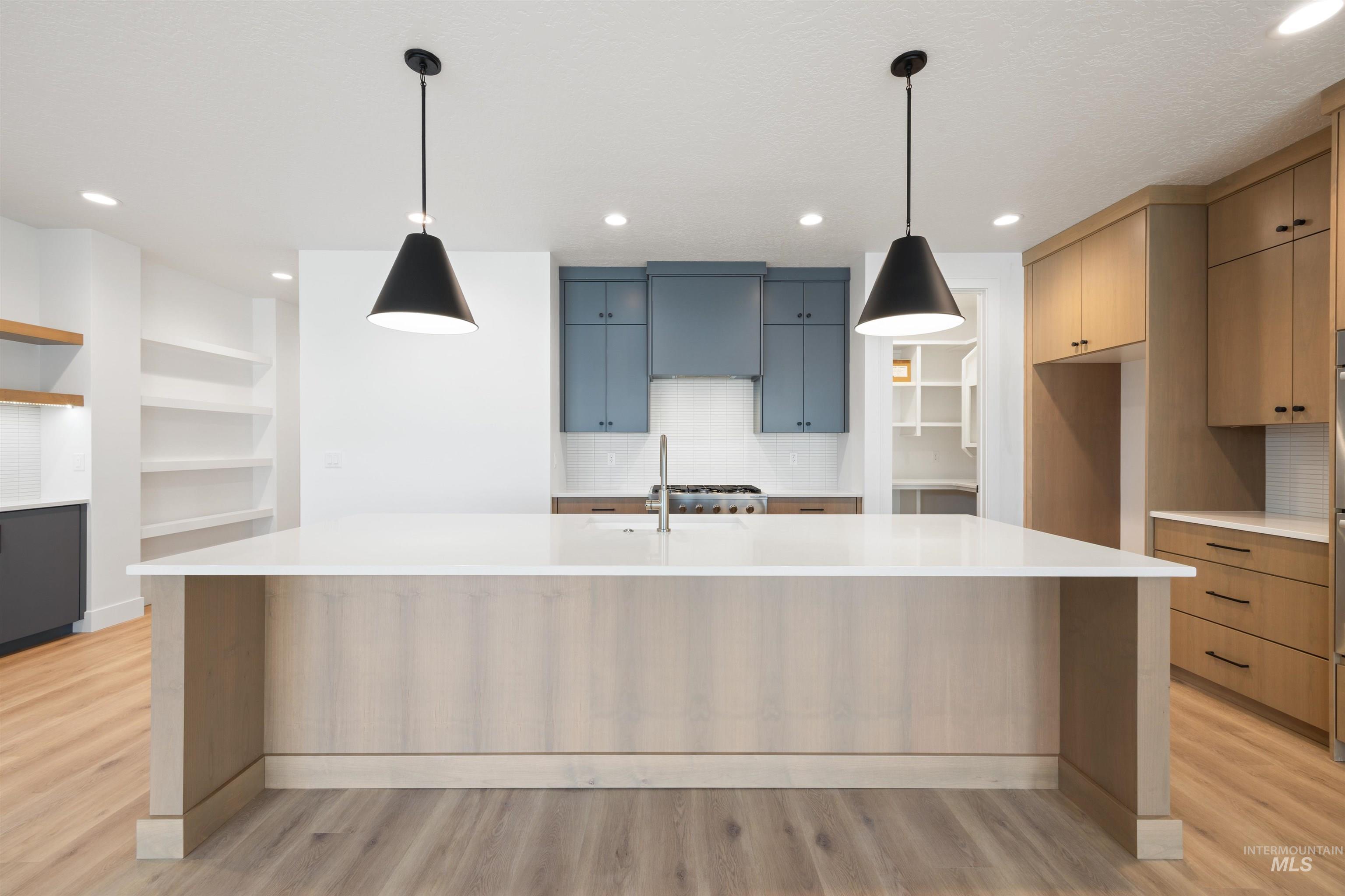 Kitchen featuring tasteful backsplash, a large island with sink, decorative light fixtures, and light wood-type flooring