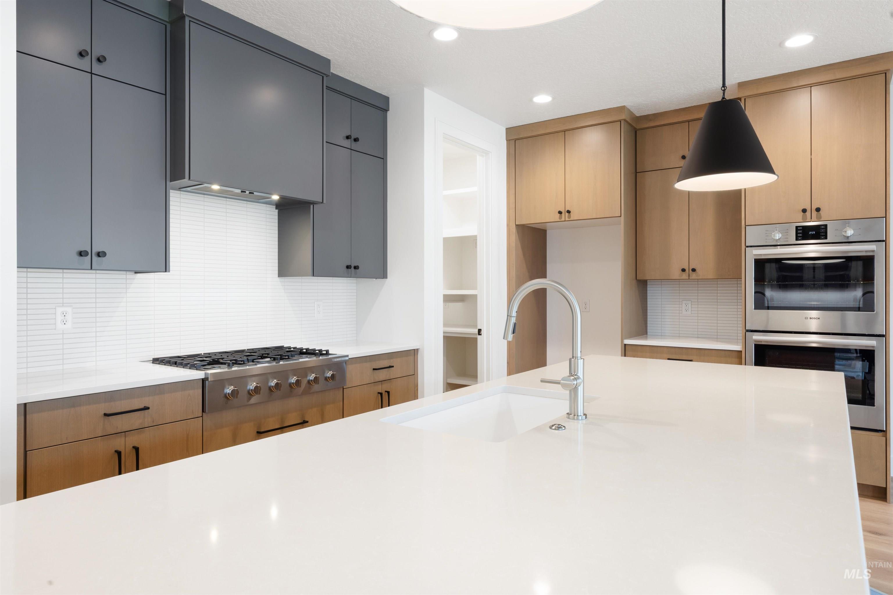 Kitchen with decorative backsplash, pendant lighting, stainless steel appliances, and light stone countertops