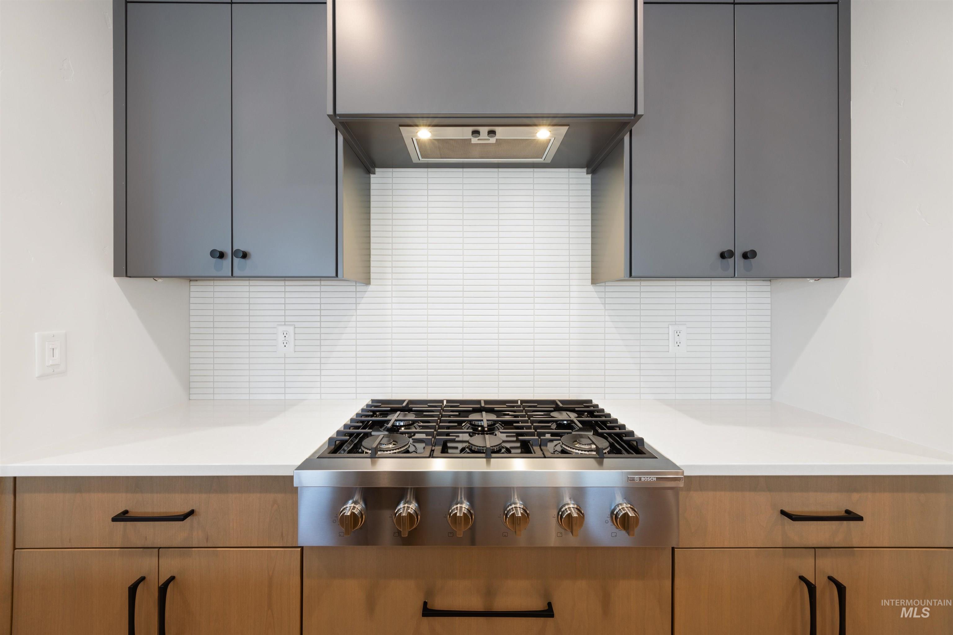 Kitchen featuring stainless steel gas cooktop, backsplash, and exhaust hood