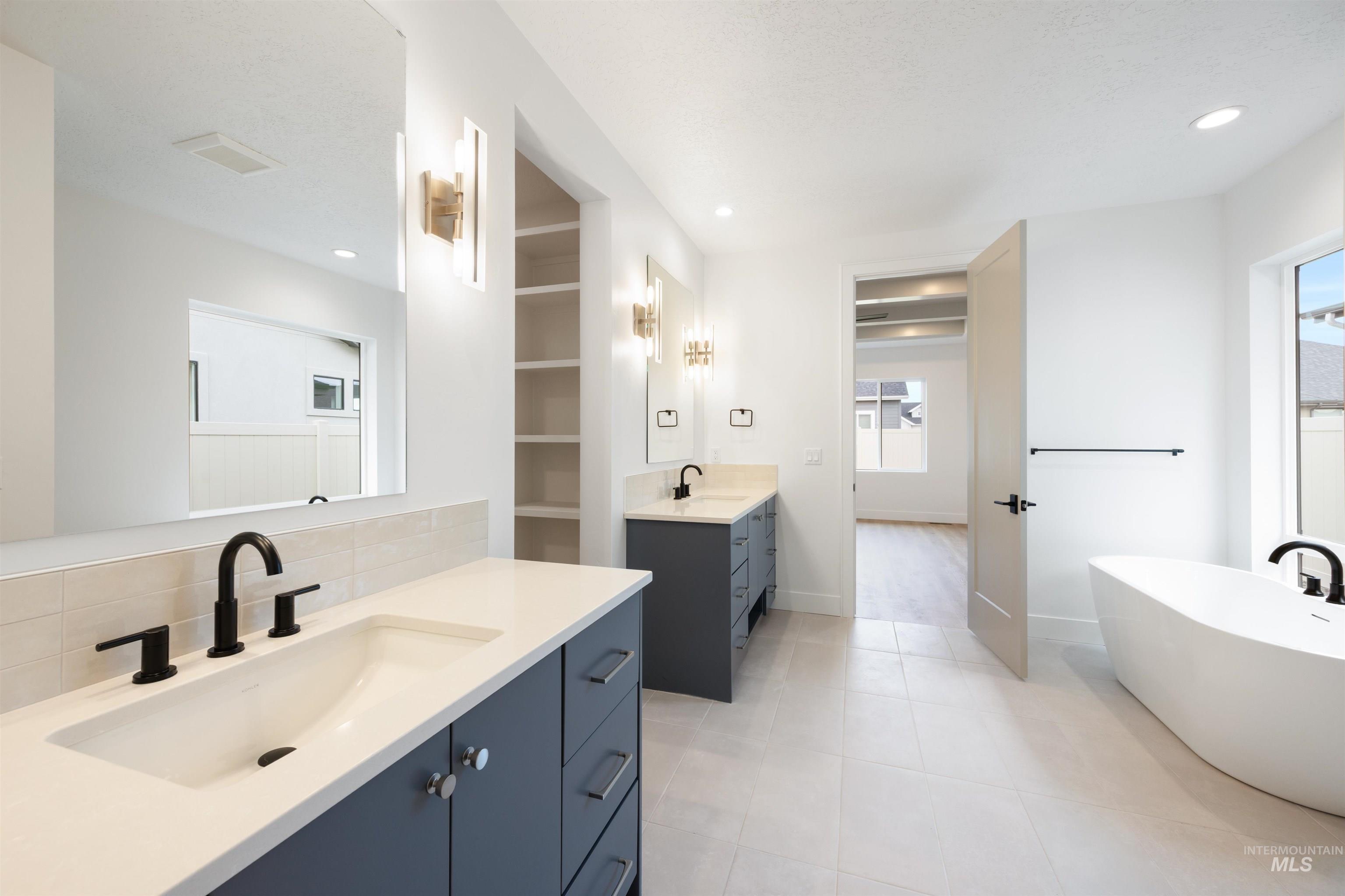 Bathroom with a freestanding bath, two vanities, tasteful backsplash, light tile patterned floors, and recessed lighting