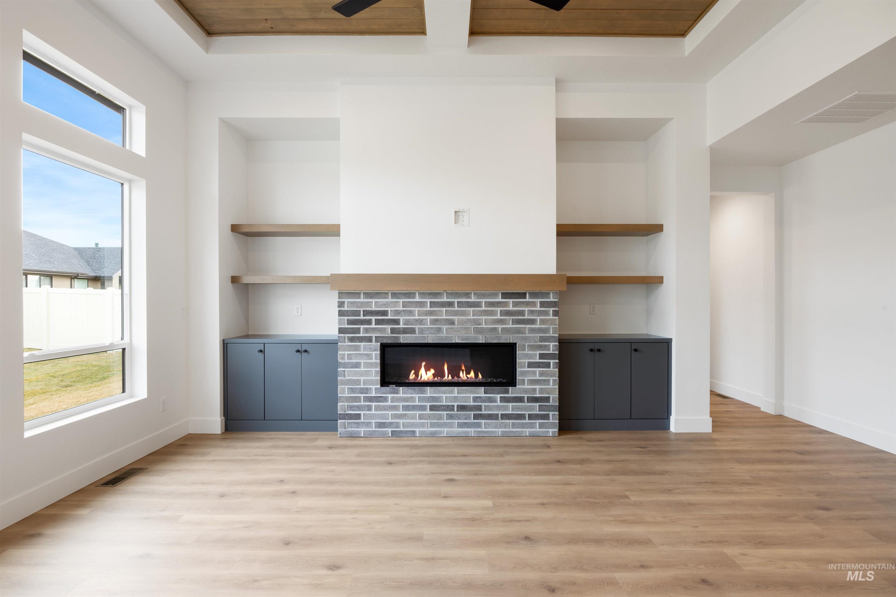 Unfurnished living room featuring built in shelves, light wood finished floors, a glass covered fireplace, wooden ceiling, and ceiling fan