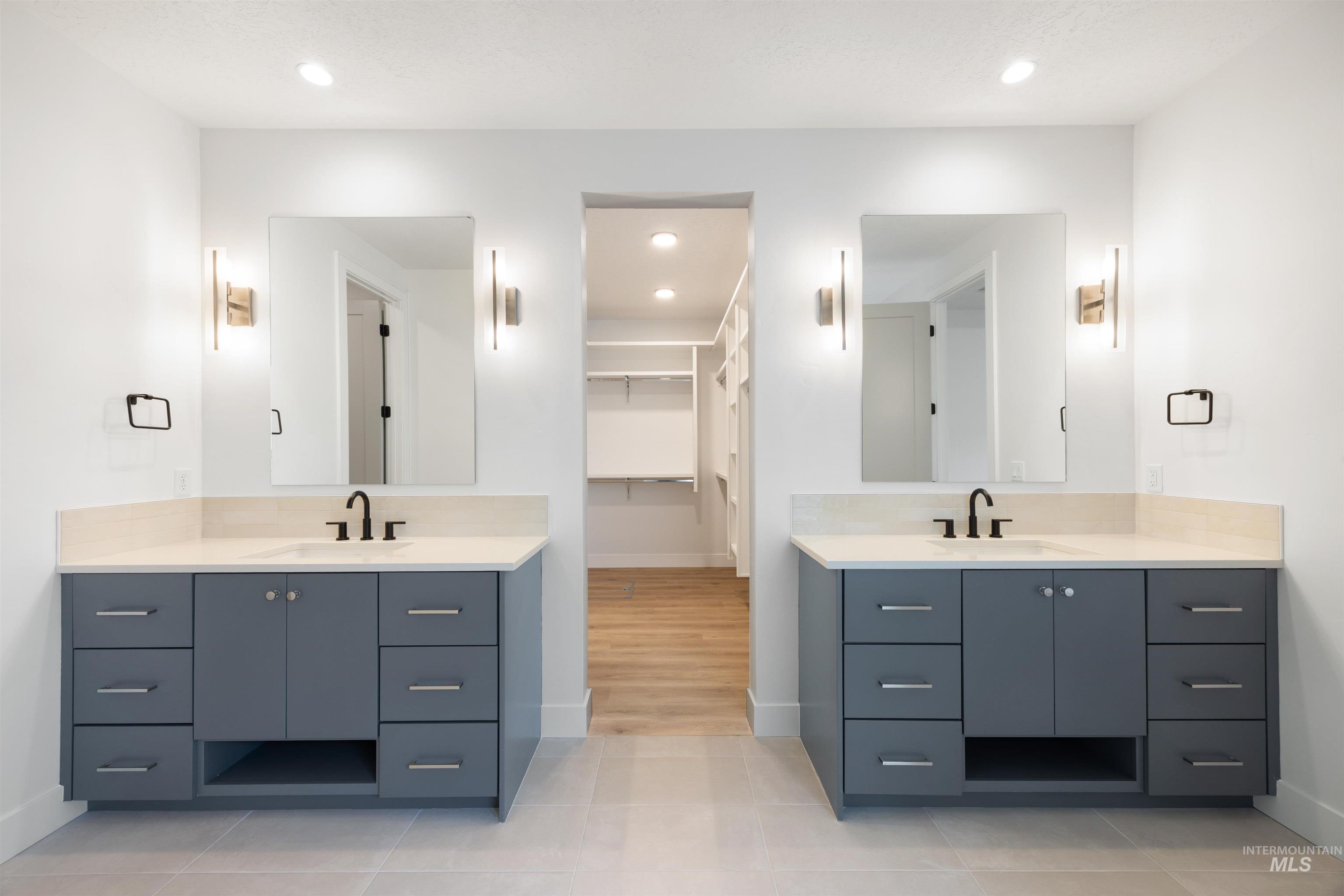 Full bathroom with a spacious closet, two vanities, recessed lighting, and light tile patterned floors