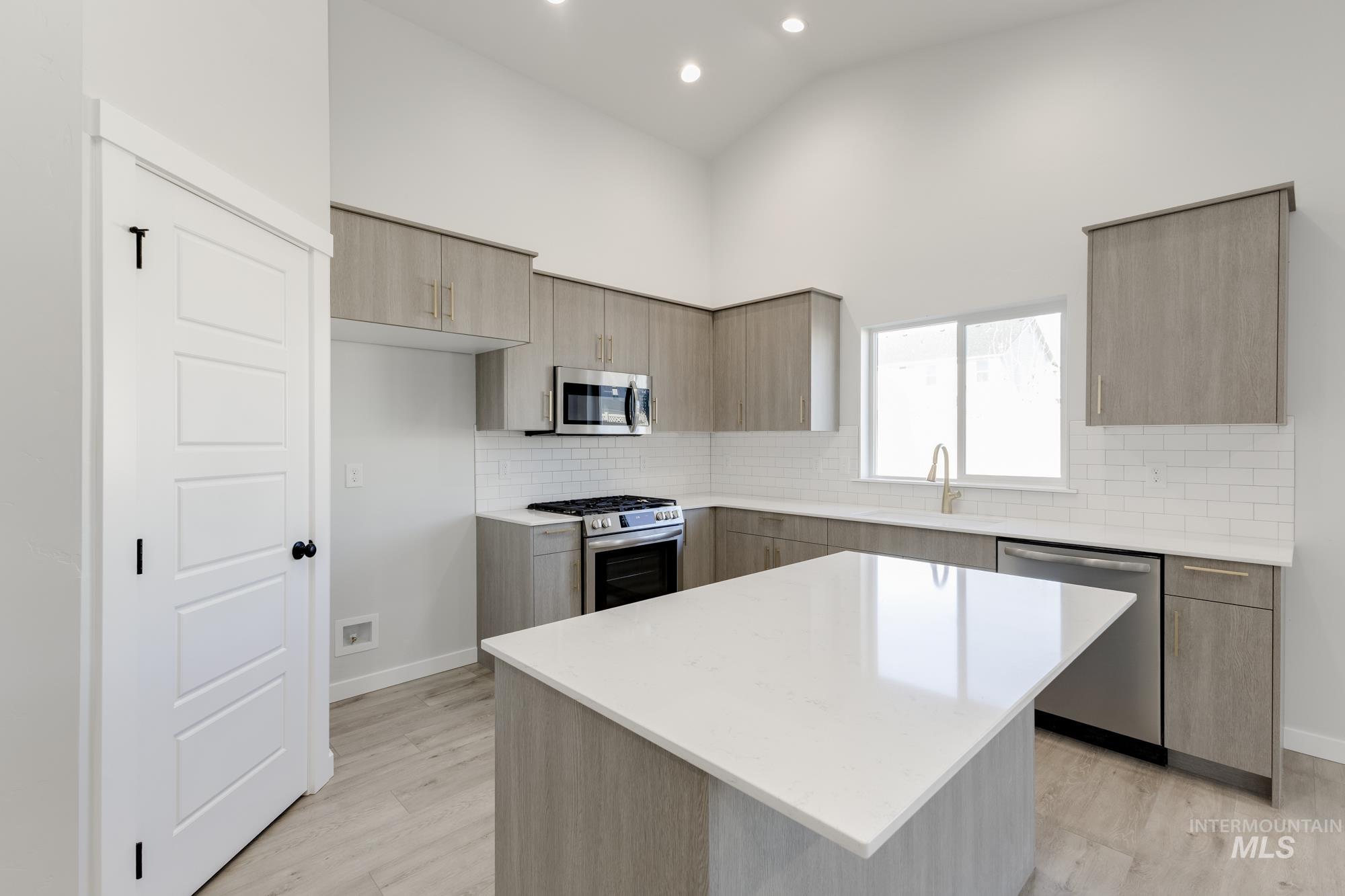 Kitchen featuring modern cabinets, tasteful backsplash, appliances with stainless steel finishes, a center island, and light stone countertops