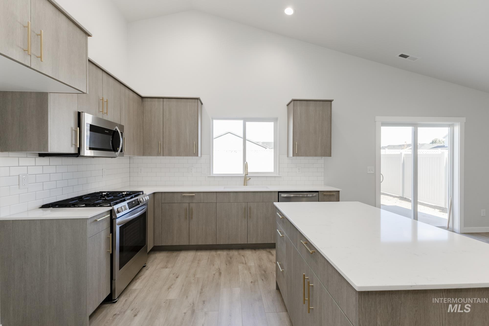 Kitchen with appliances with stainless steel finishes, lofted ceiling, modern cabinets, tasteful backsplash, and light stone countertops