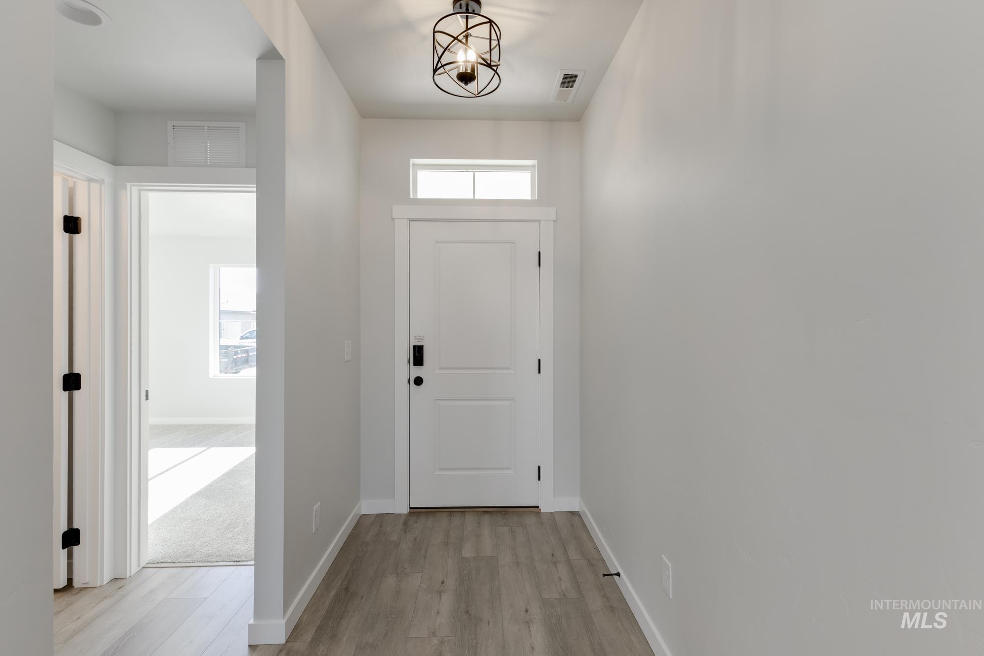 Doorway to outside with healthy amount of natural light, wood finished floors, and a chandelier