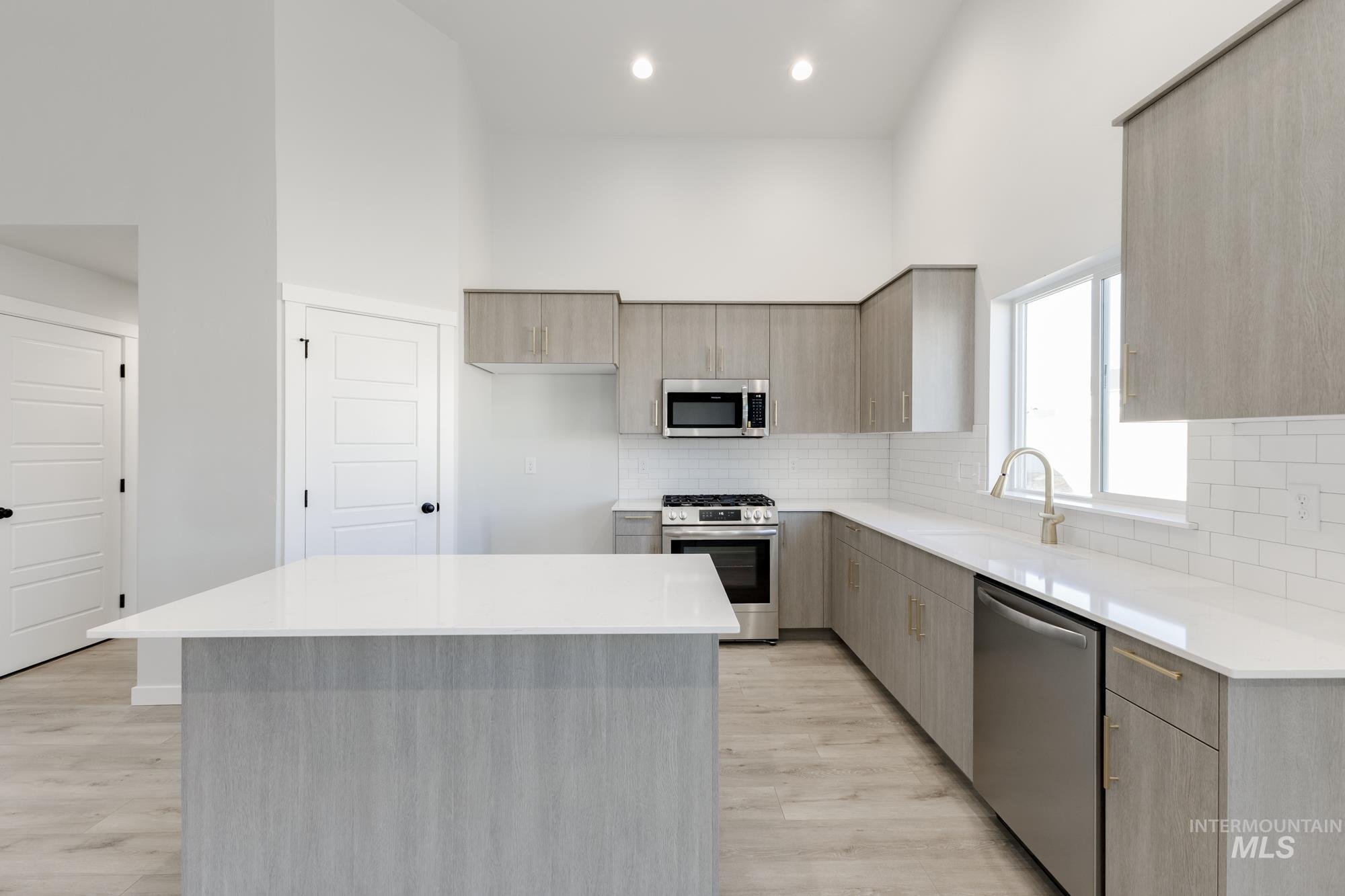 Kitchen with modern cabinets, a kitchen island, appliances with stainless steel finishes, light stone counters, and a high ceiling