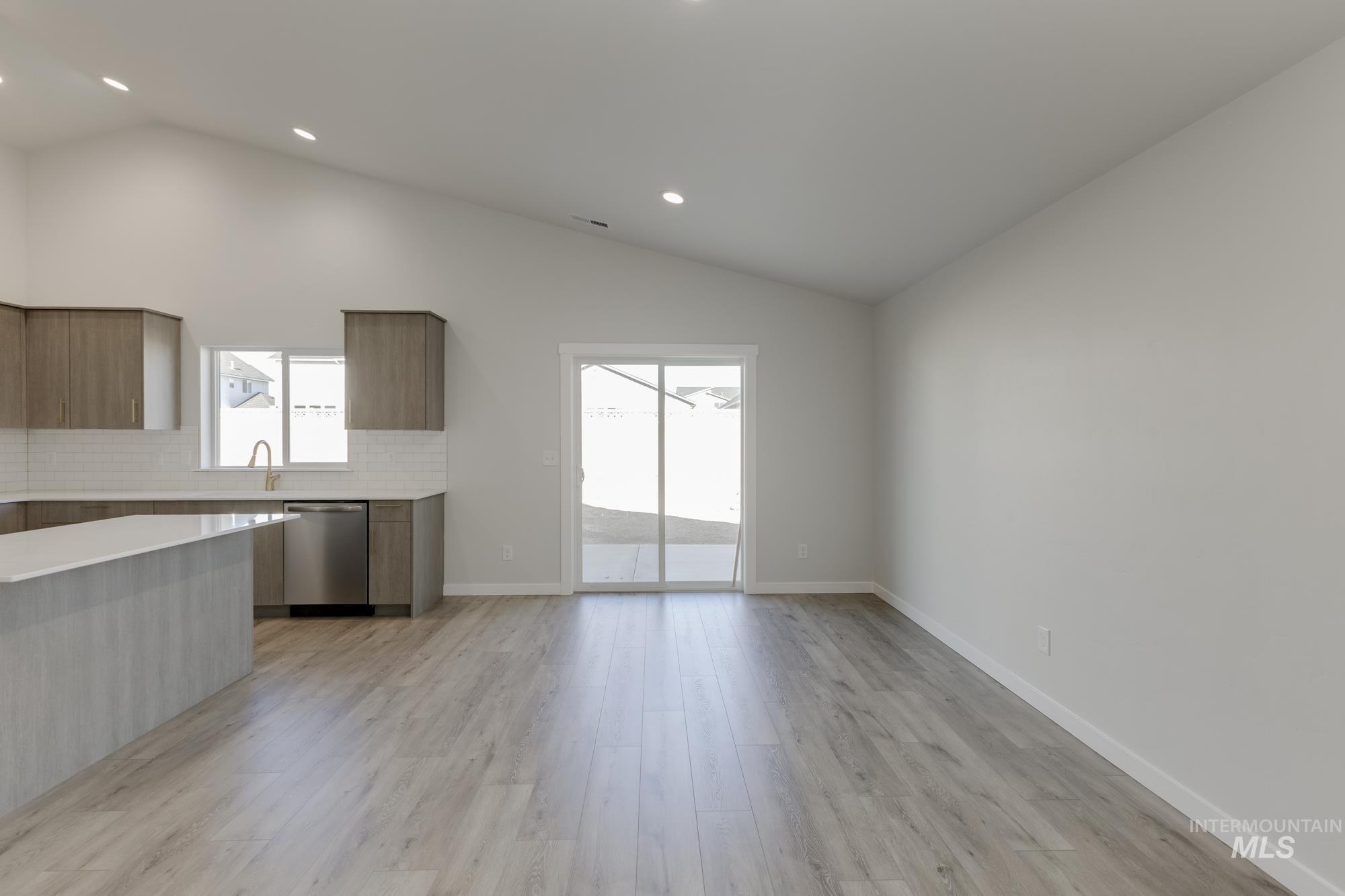 Kitchen with modern cabinets, vaulted ceiling, backsplash, light wood-style flooring, and dishwasher
