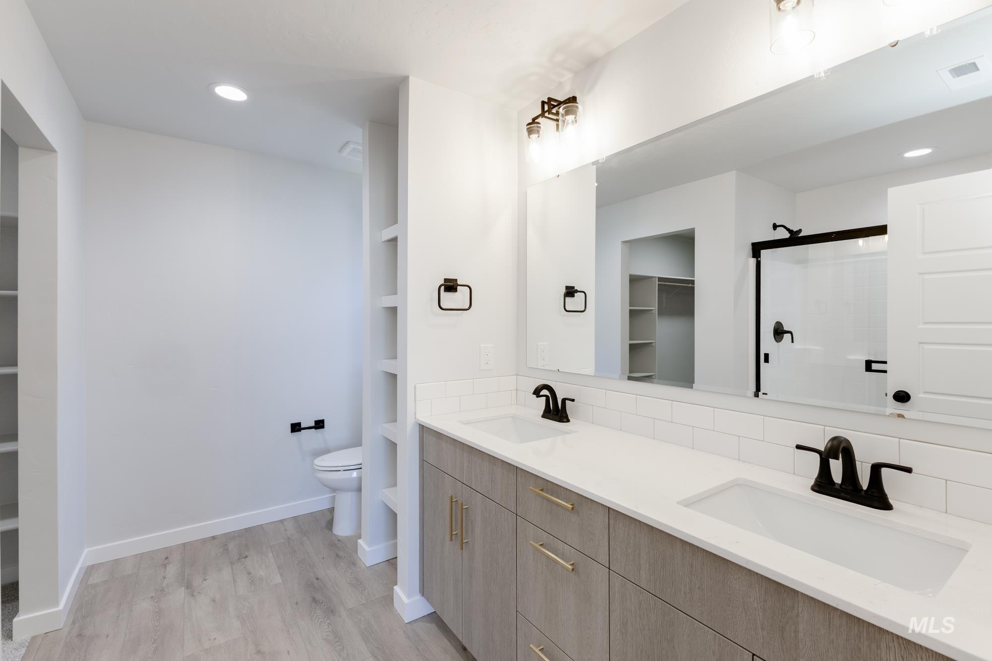 Full bath featuring a spacious closet, a stall shower, recessed lighting, double vanity, and light wood finished floors
