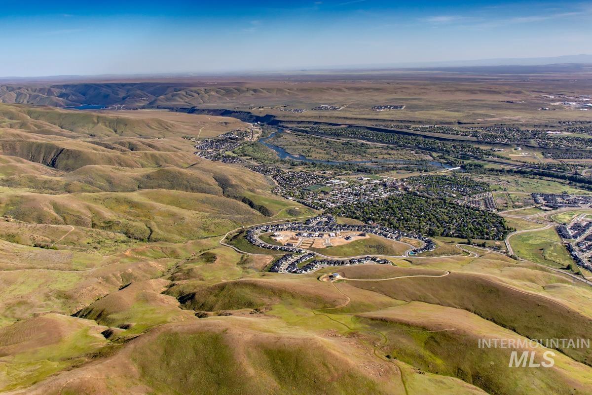 Expansive aerial capturing rolling hills, a winding river, and a residential community nestled within a verdant valley