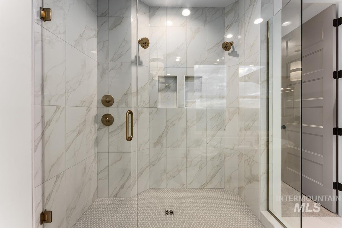 Frameless glass shower enclosure featuring large-format marble-look wall tiles, hexagonal floor tiles, dual shower heads, and integrated recessed shelving