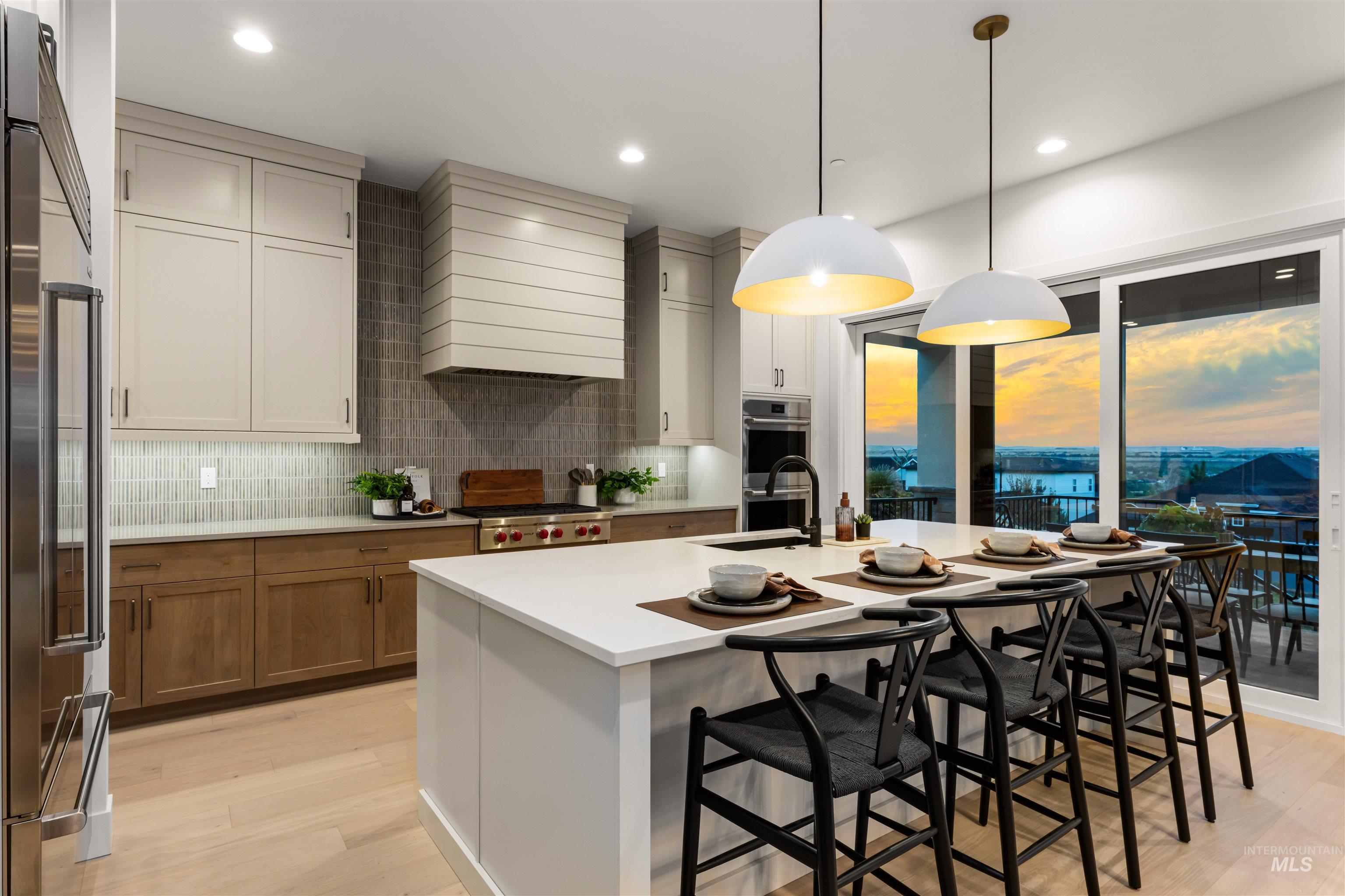Open-concept kitchen featuring an oversized island with seating, pendant lighting, stainless steel appliances, a tile backsplash, and sliding glass doors to outdoor space