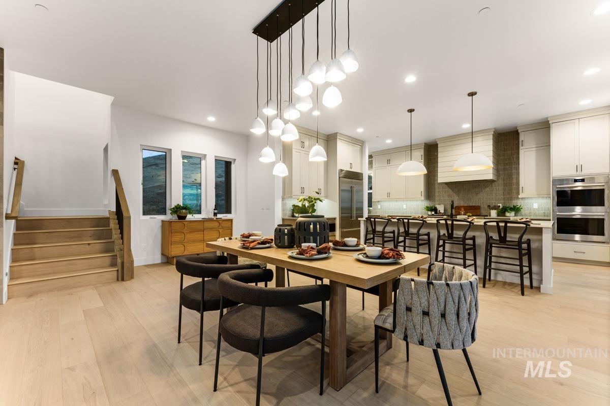 Open-concept living space featuring light wood-finish flooring, a contemporary dining area with an elongated pendant light fixture, and a kitchen with light-toned cabinetry and stainless steel appliances