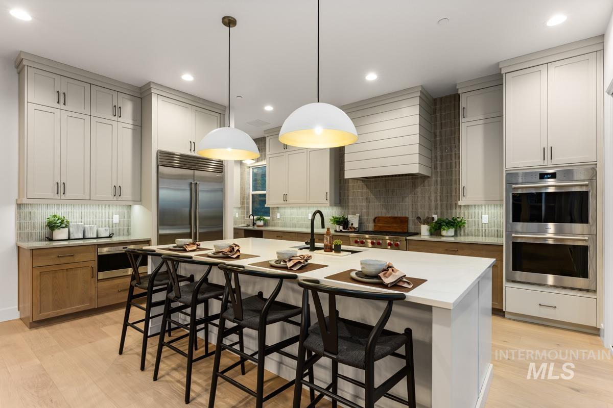 Spacious kitchen featuring a large central island with seating for four, light wood-finish flooring, two-tone cabinetry, stainless steel appliances, and a tiled backsplash