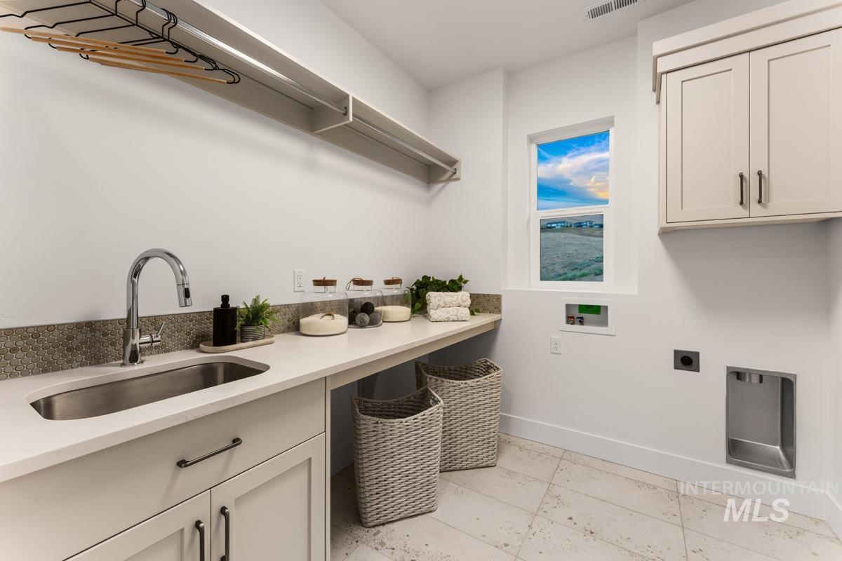 Laundry room featuring a stainless steel sink, quartz countertop, mosaic tile backsplash, and light wood-finish cabinetry