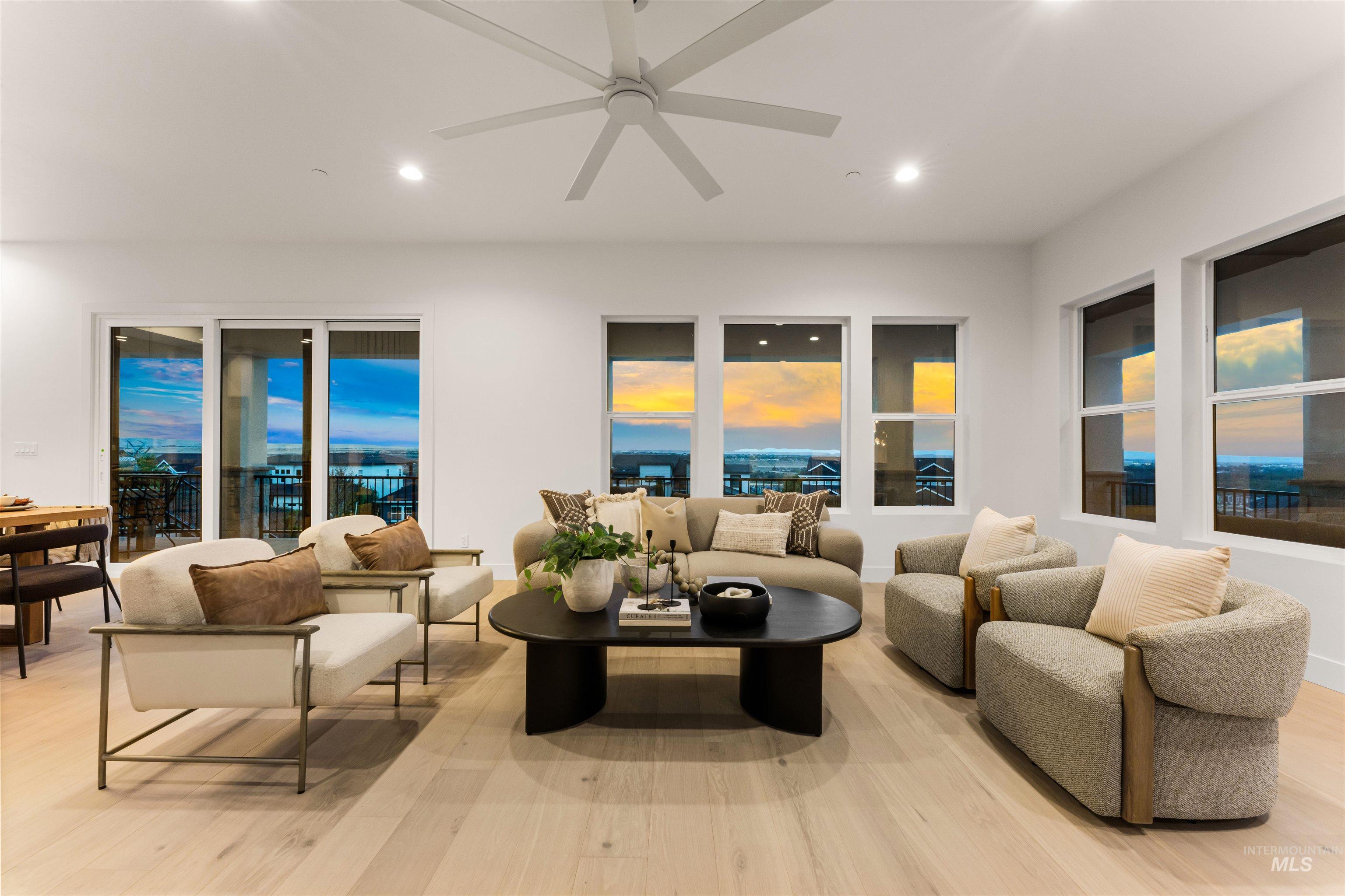 Spacious living area featuring light wood-finish flooring, ample natural light through multiple windows, recessed lighting, and a contemporary ceiling fan