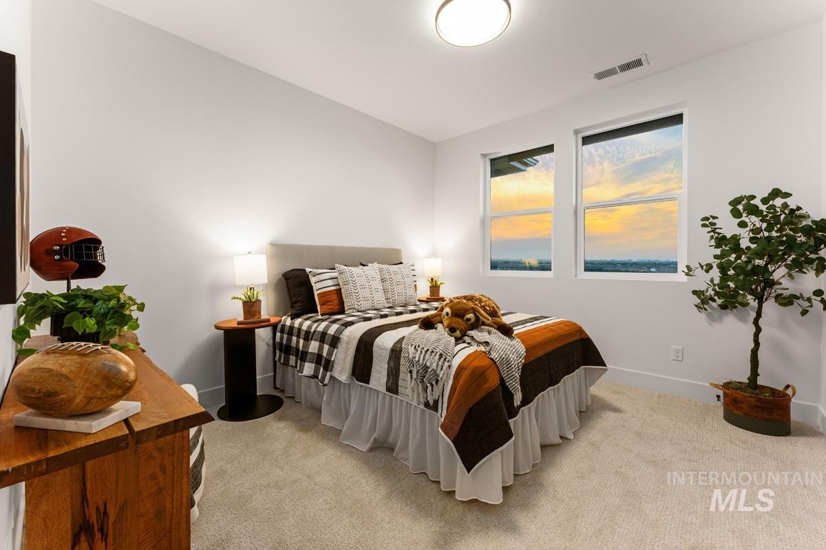 Bright bedroom featuring two large windows, overhead lighting, plush carpet, and white baseboards