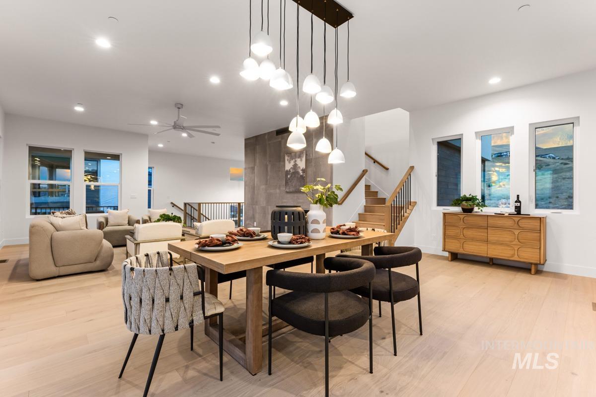 Open-concept living area featuring a modern dining chandelier, wood-finish flooring, a built-in staircase with black metal balusters, recessed lighting, and large windows