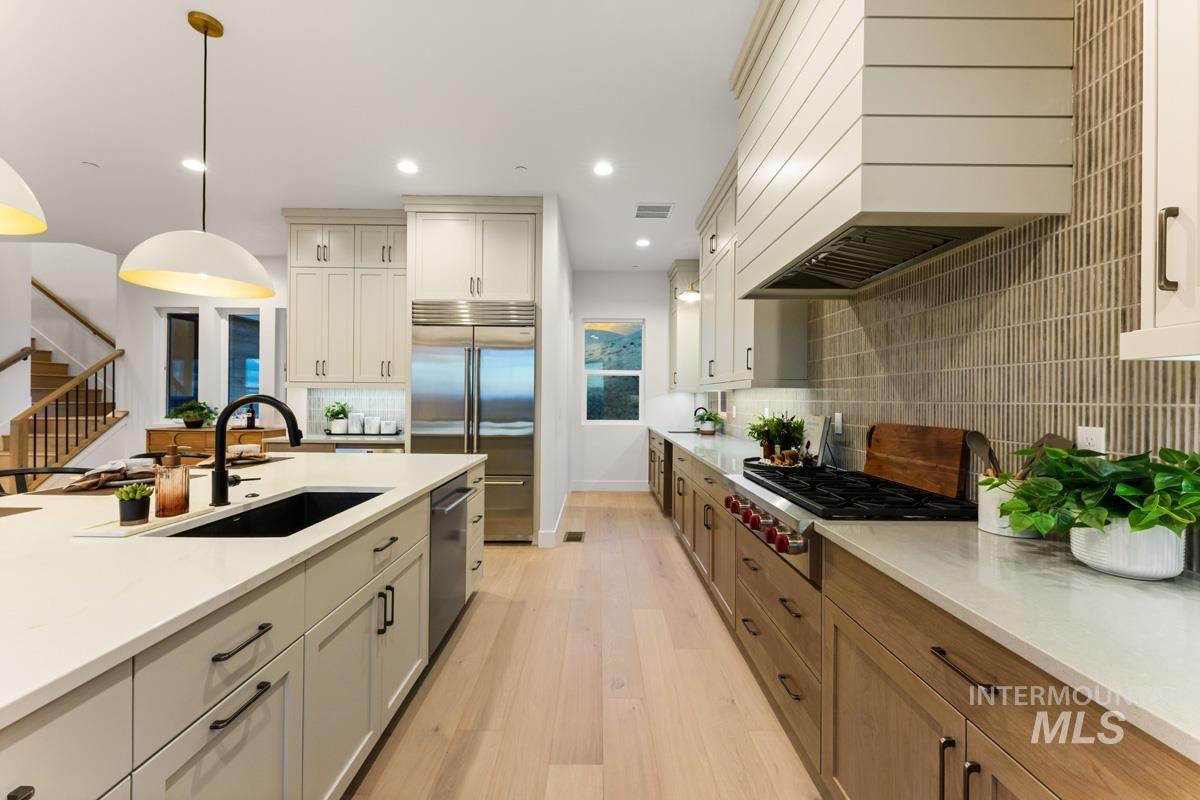 Gourmet kitchen featuring a large island with a black sink, light-toned cabinetry, stainless steel appliances, and wood-finish flooring