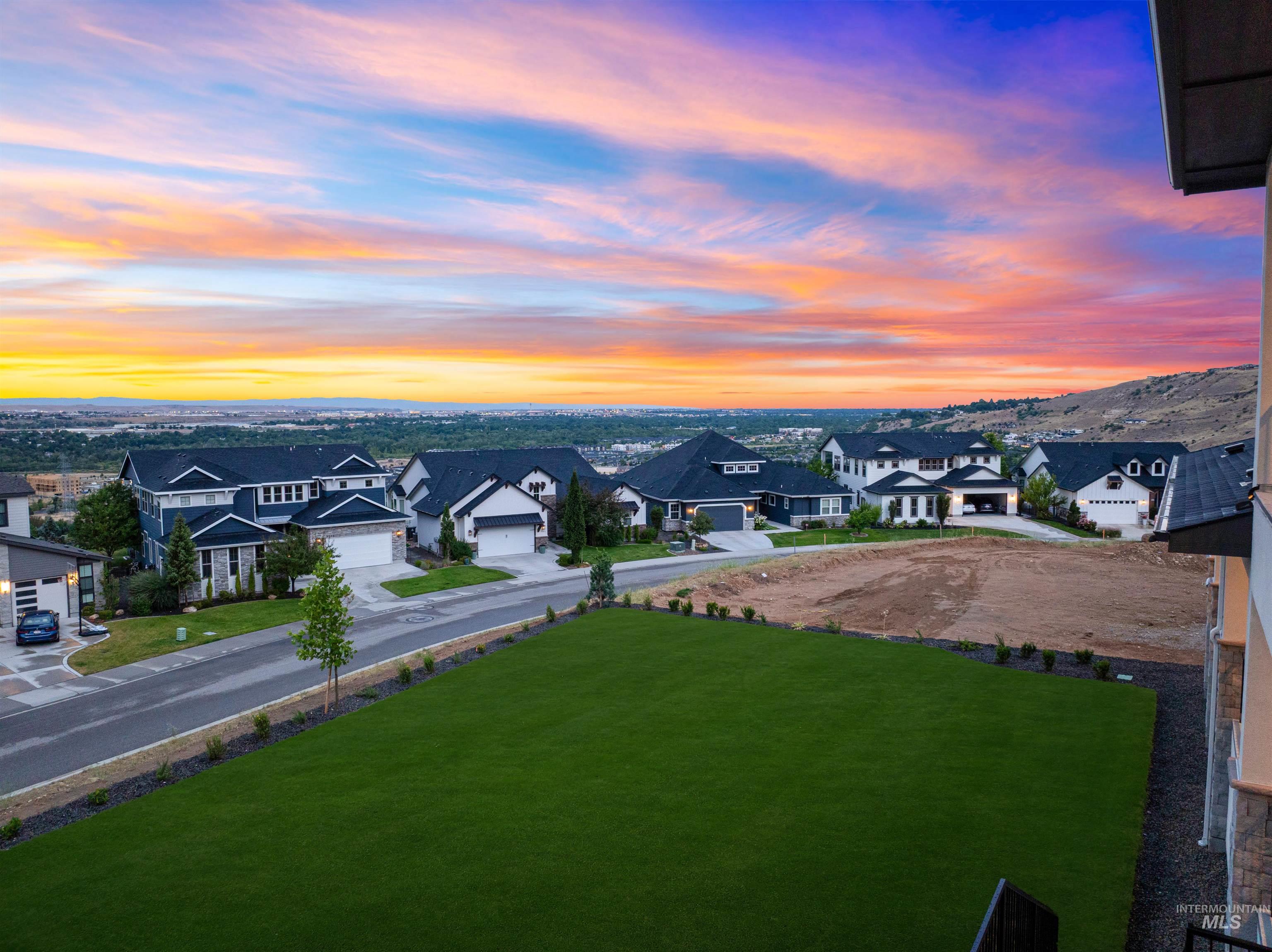 Expansive green lawn area with a backdrop of a residential community, distant hills, and a colorful sky