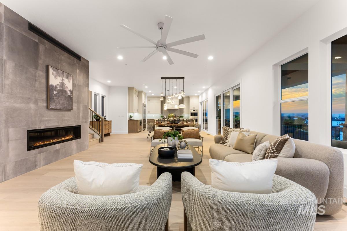 Open concept living space featuring wood-finish flooring, a linear fireplace with a stone-look surround, recessed lighting, a ceiling fan, and large windows