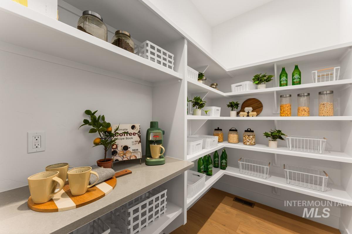 Walk-in pantry featuring extensive white shelving, a light-toned countertop surface, and wood-finish flooring