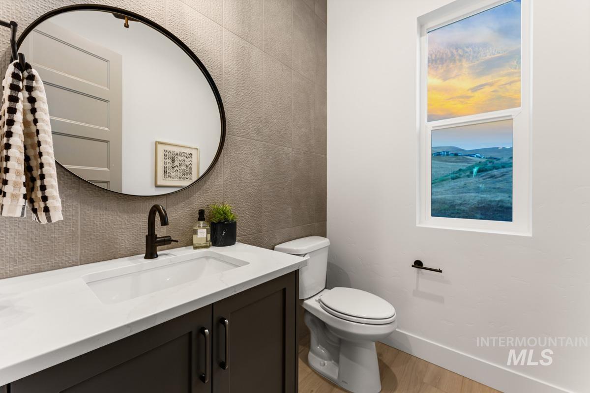 Powder room featuring a dark wood vanity with a white countertop and integrated sink, a large circular mirror with a black frame, textured wall tiling, and light wood-finish flooring