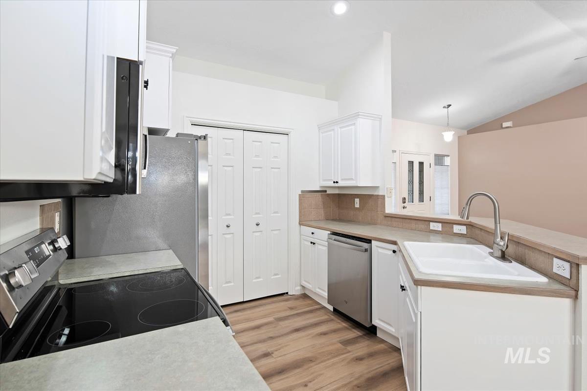Kitchen featuring white cabinetry, stainless steel appliances, light countertops, light wood finished floors, and decorative light fixtures