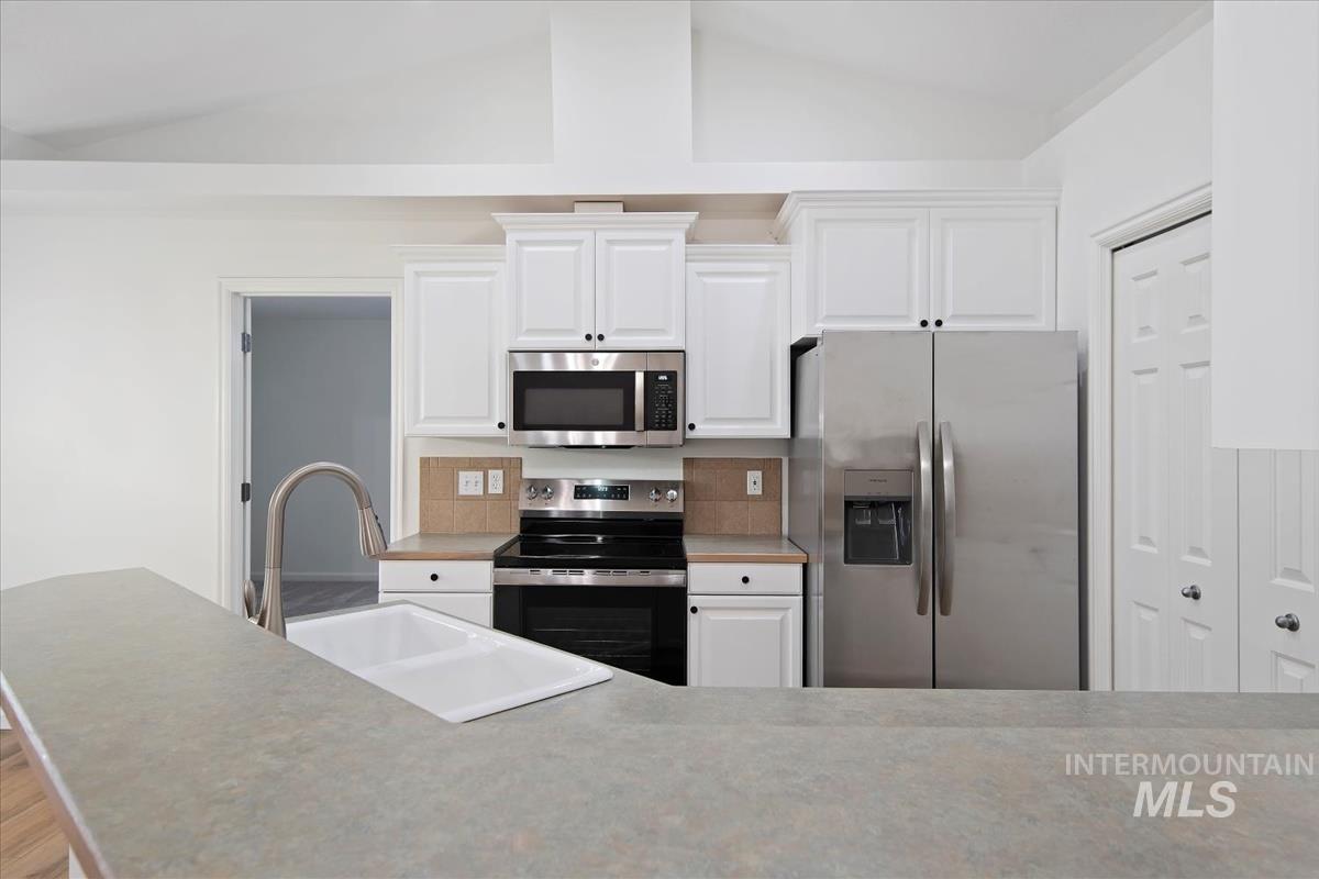 Kitchen with appliances with stainless steel finishes, light countertops, white cabinetry, and vaulted ceiling