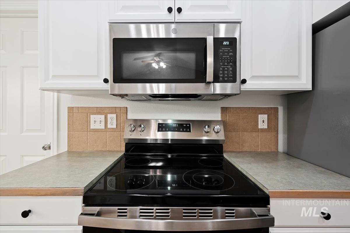 Kitchen view of appliances with stainless steel finishes, light countertops, white cabinets, and tasteful backsplash