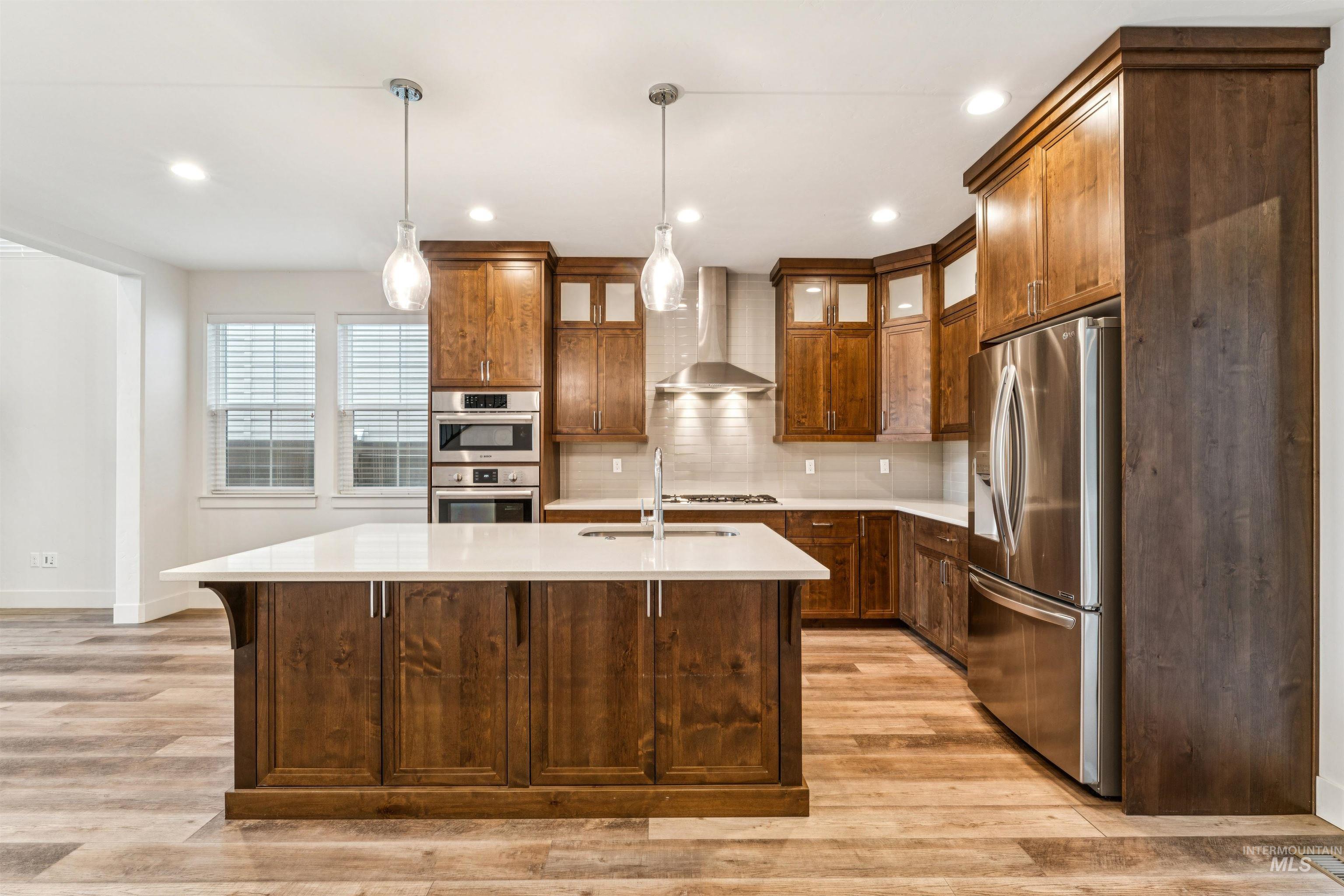 Kitchen with stainless steel appliances, pendant lighting, light quartz countertops, tasteful backsplash, and wall chimney range hood