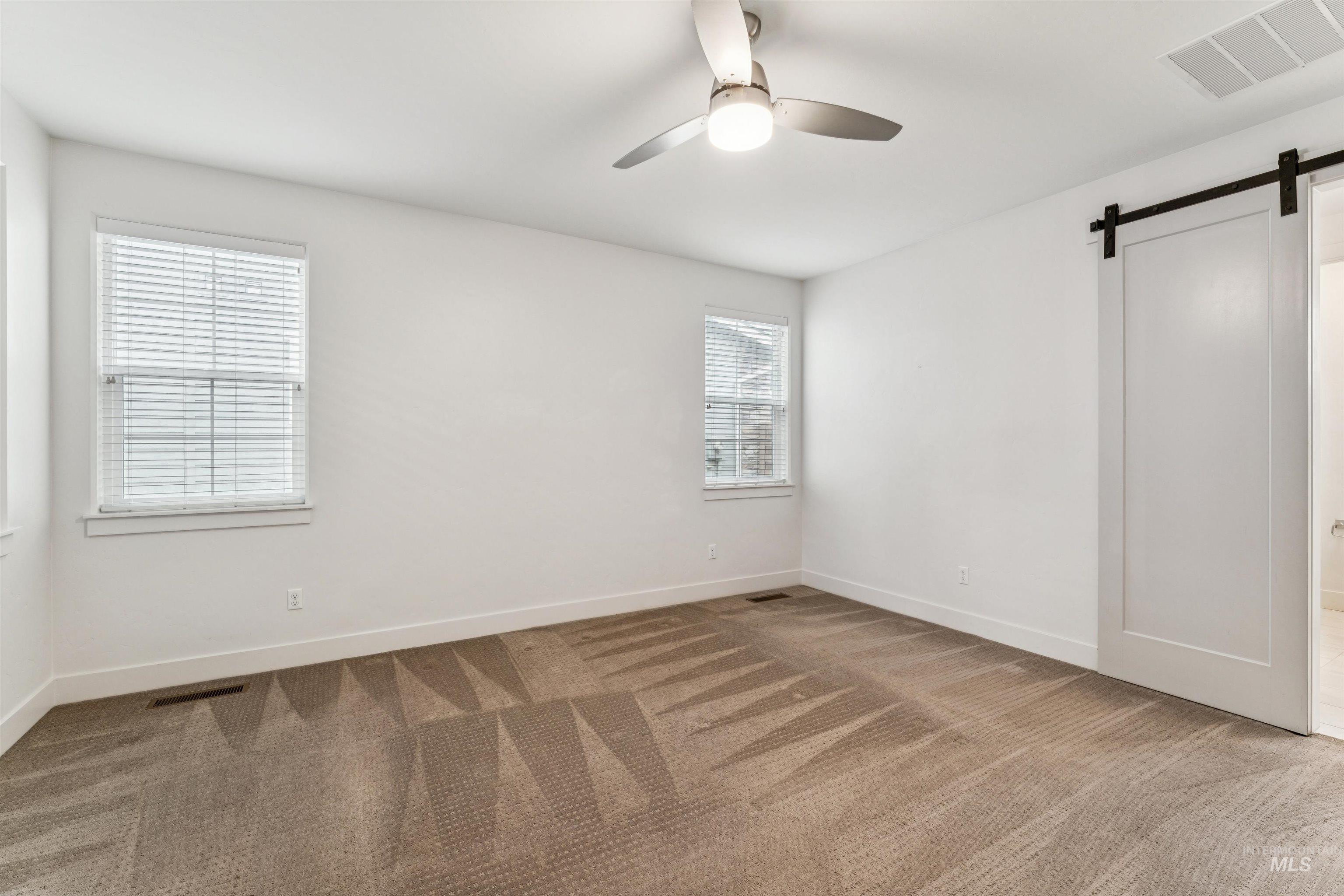 Primary bedroom featuring a barn door and ceiling fan
