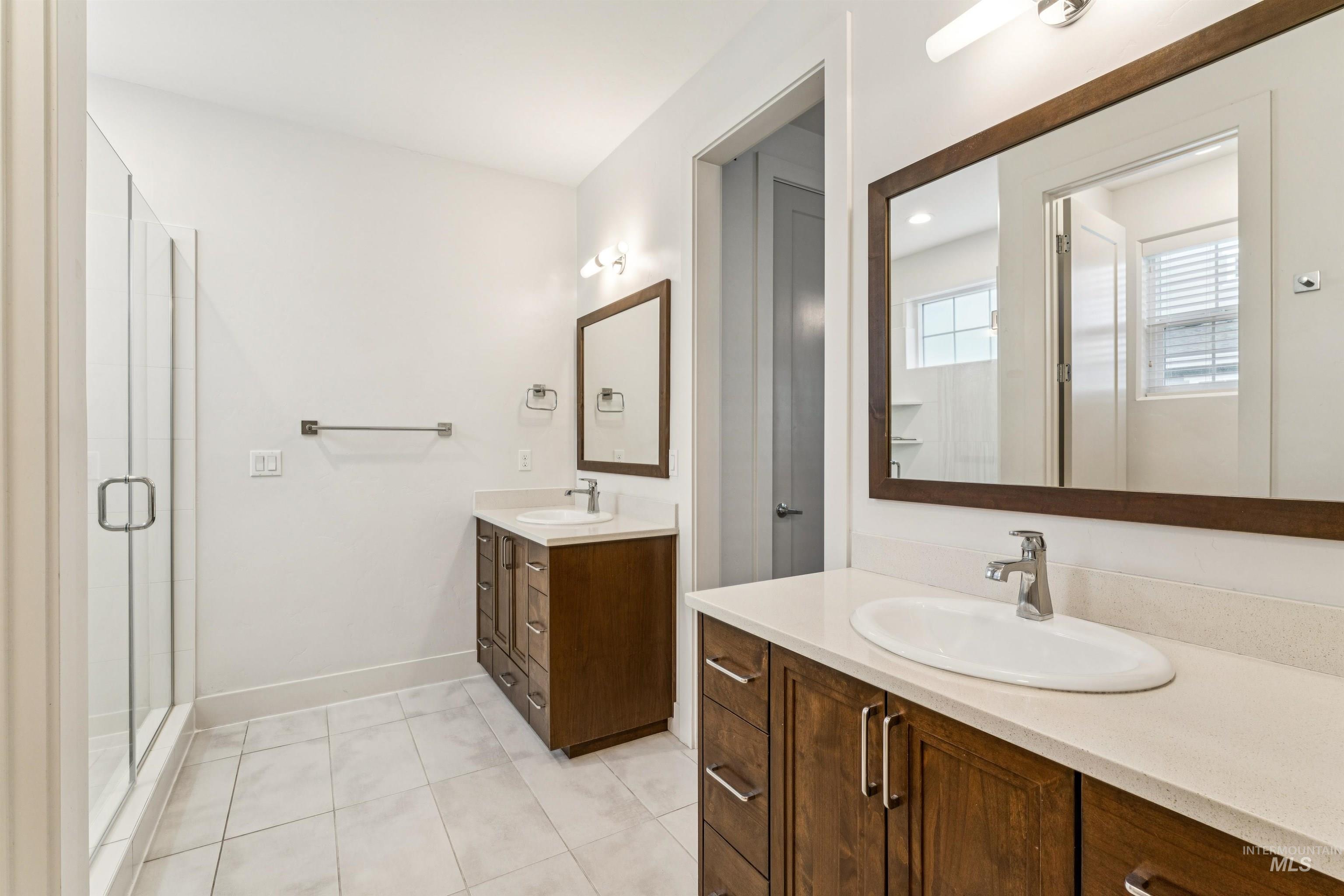 Bathroom with two vanities, a stall shower and light tile patterned floors