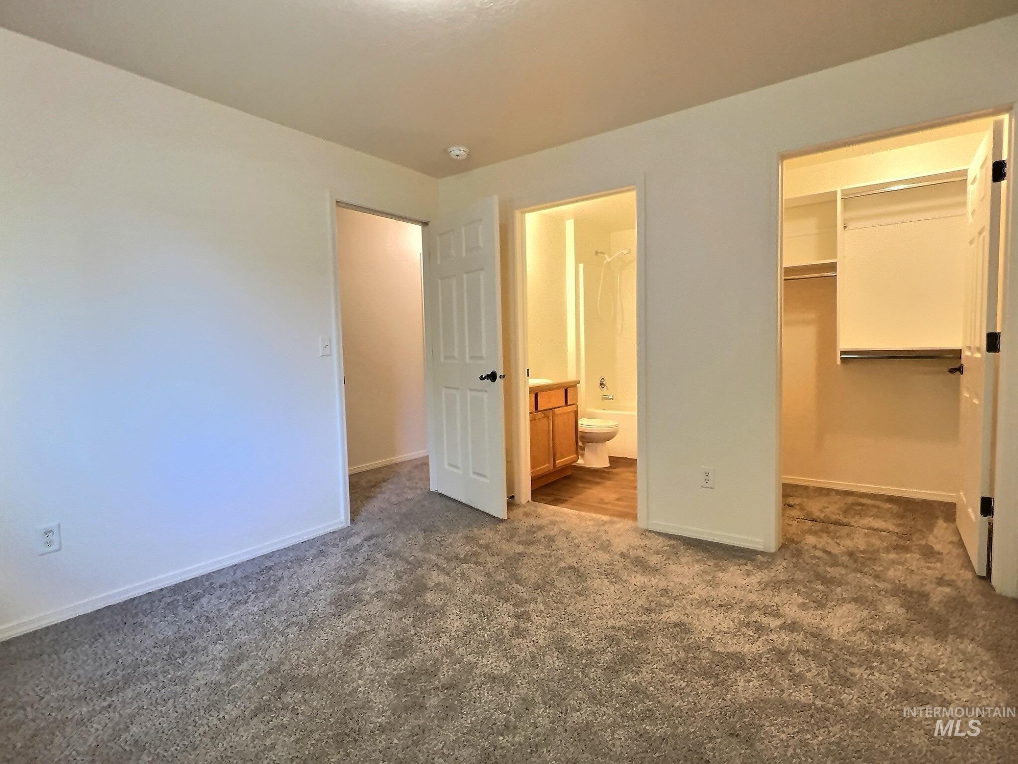 Unfurnished bedroom featuring a walk in closet, dark colored carpet, and ensuite bath